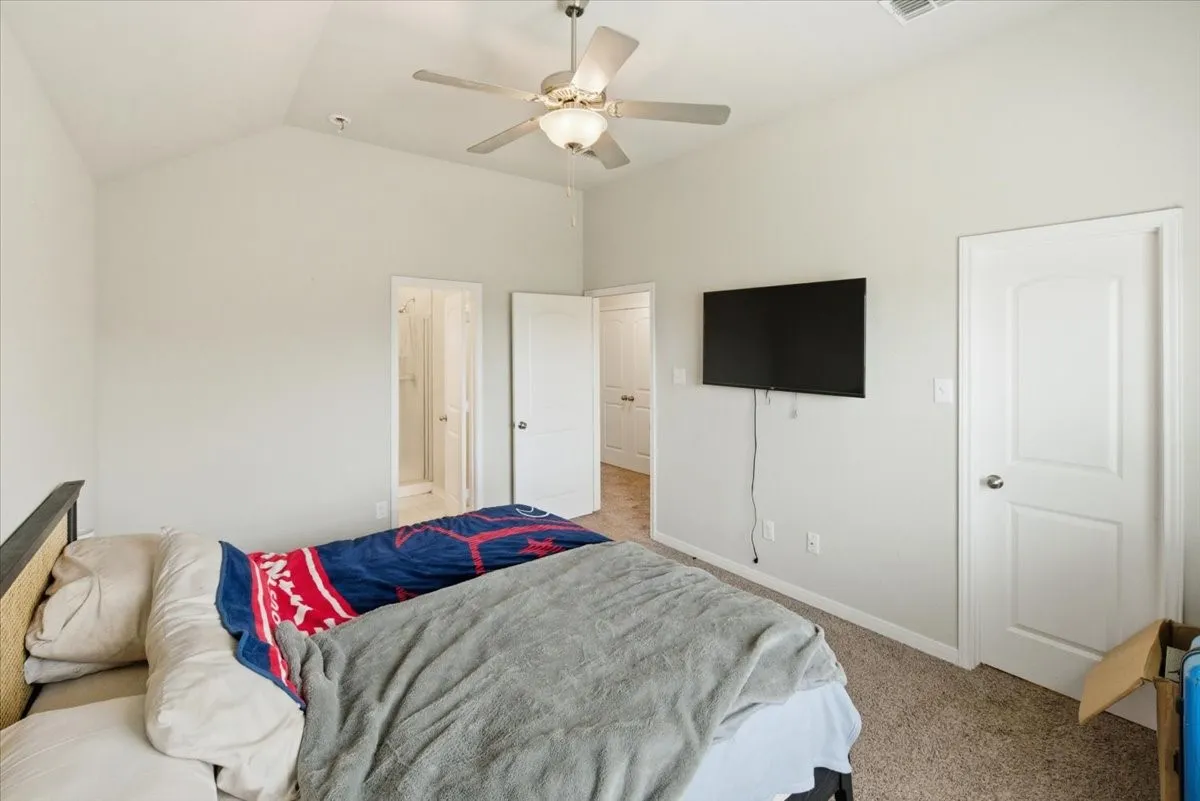 Bedroom featuring light carpet, ensuite bathroom, vaulted ceiling, and a ceiling fan