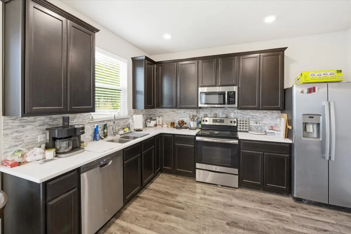 Kitchen with stainless steel appliances, dark wood finish cabinetry, light wood-look flooring, and recessed LED lighting