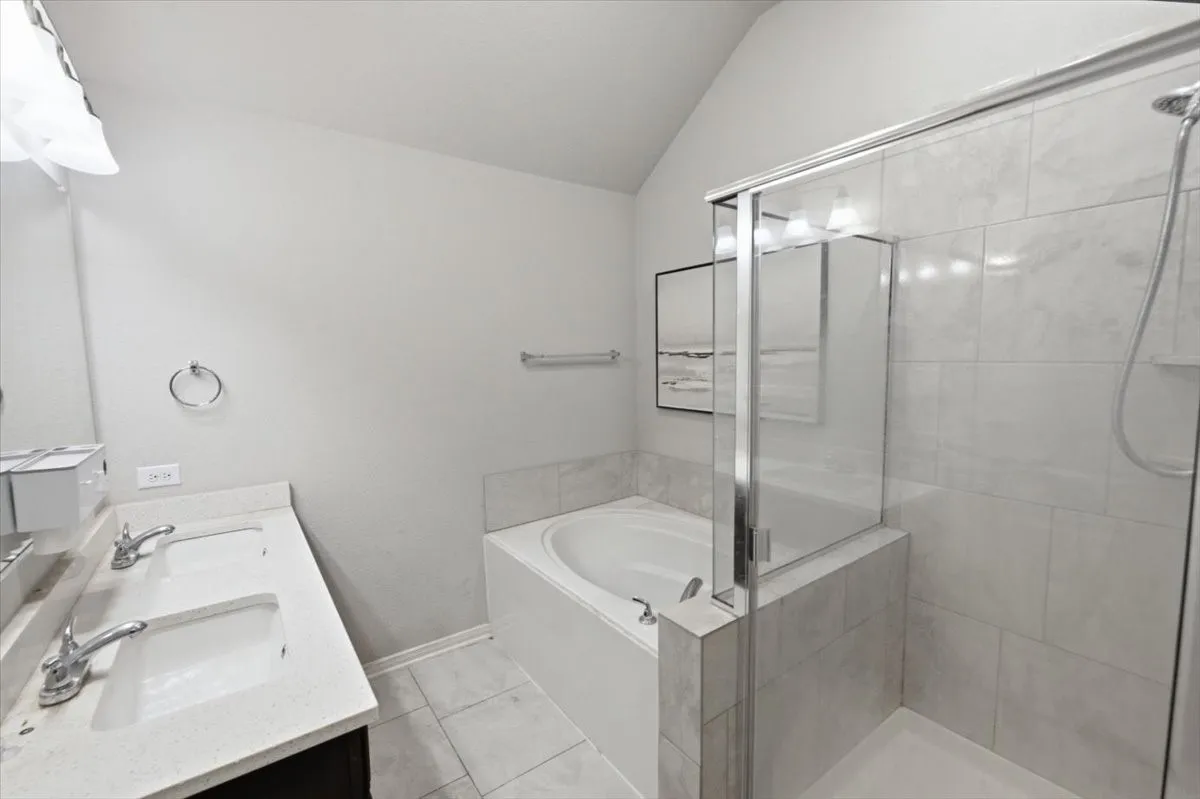 Primary bathroom with double vanity, a bath, lofted ceiling, and a large, walk-in shower