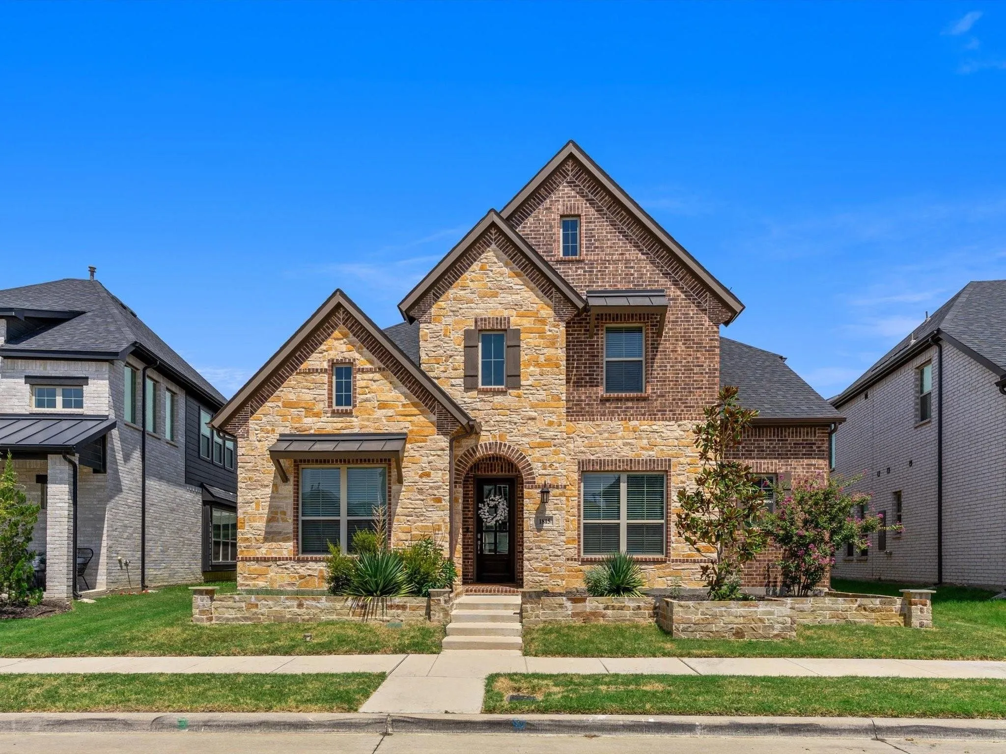 Two-story residence featuring a combination stone and brick facade, dark roofing, and shuttered windows