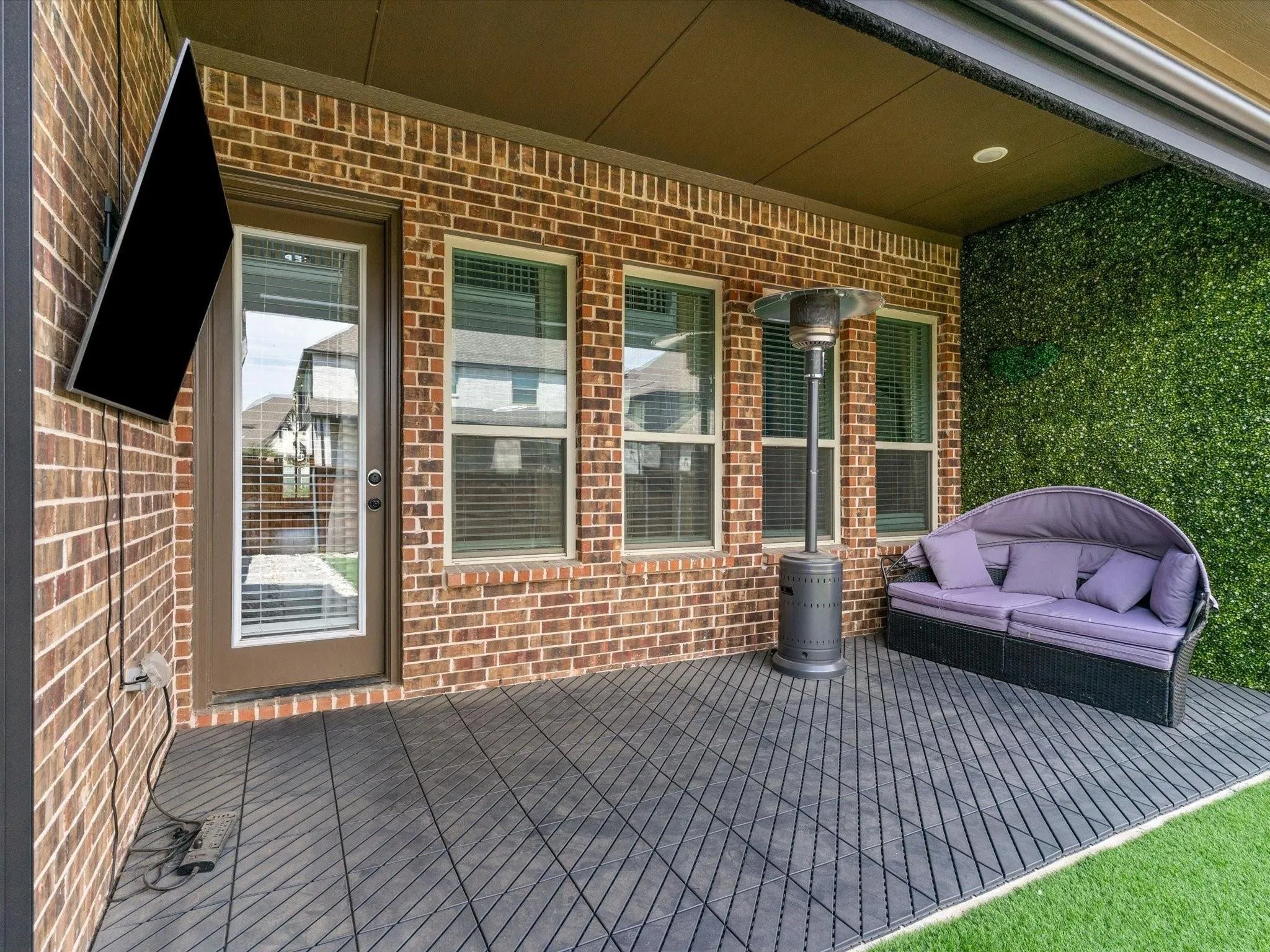 Covered outdoor patio featuring brick exterior, full-light glass door, and a wall-mounted television