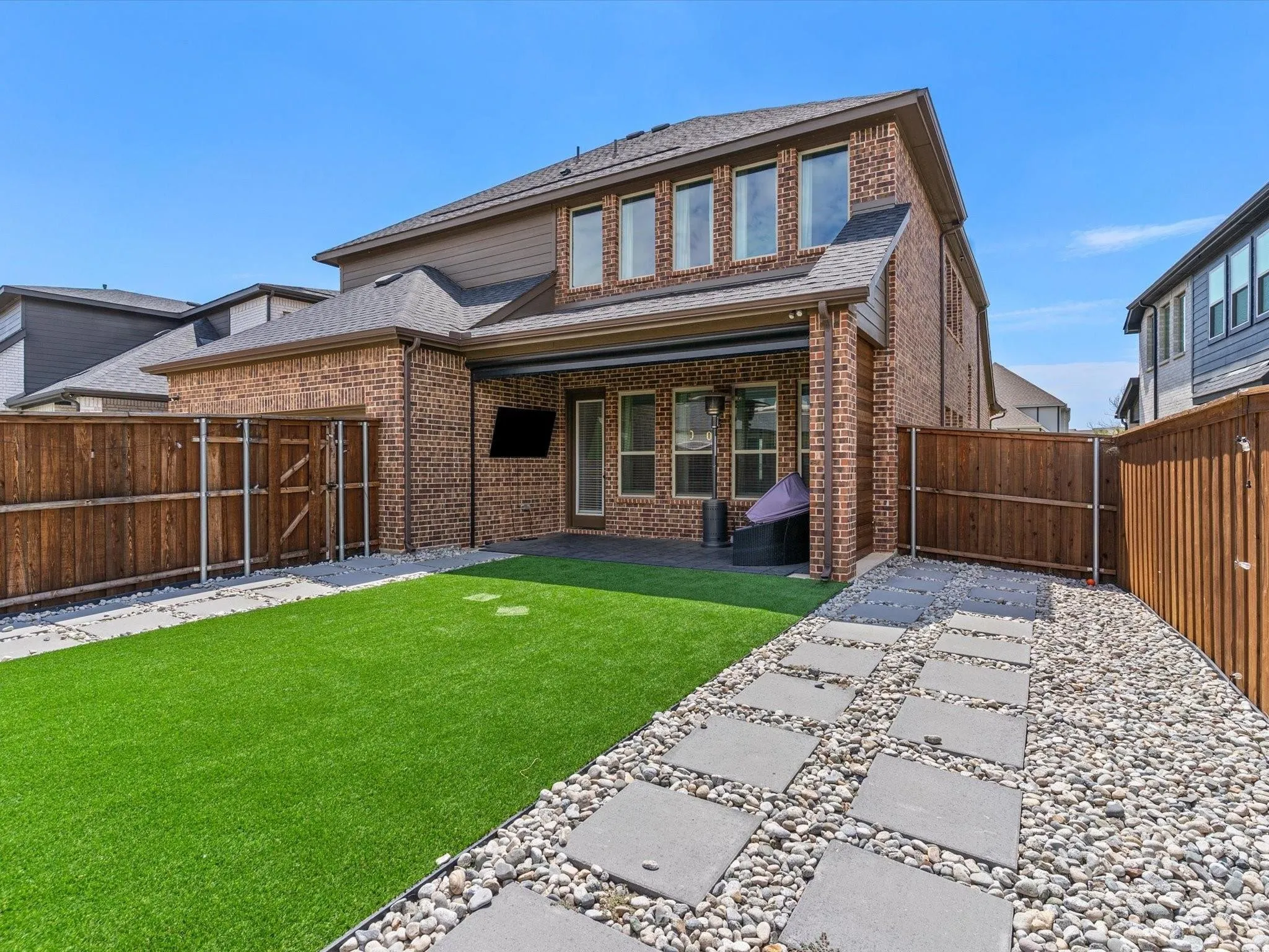 Private backyard featuring artificial turf, a stone paver pathway, and surrounding wood fencing