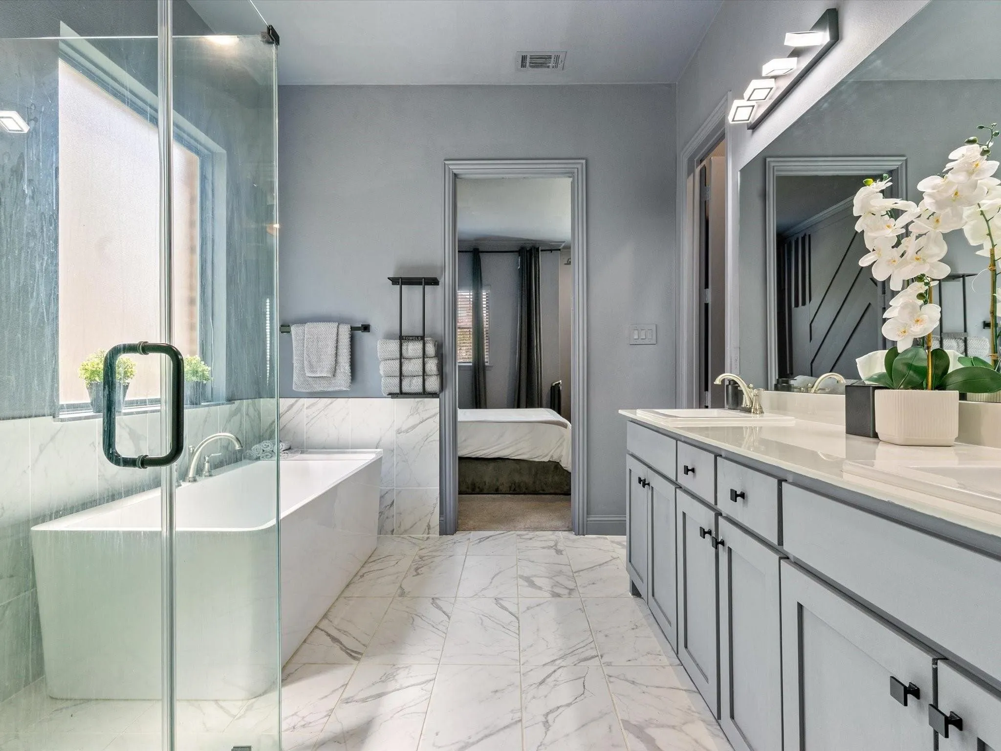Modern bathroom featuring a freestanding tub, glass-enclosed shower, dual vanity with shaker-style cabinetry, and marble-look tile flooring