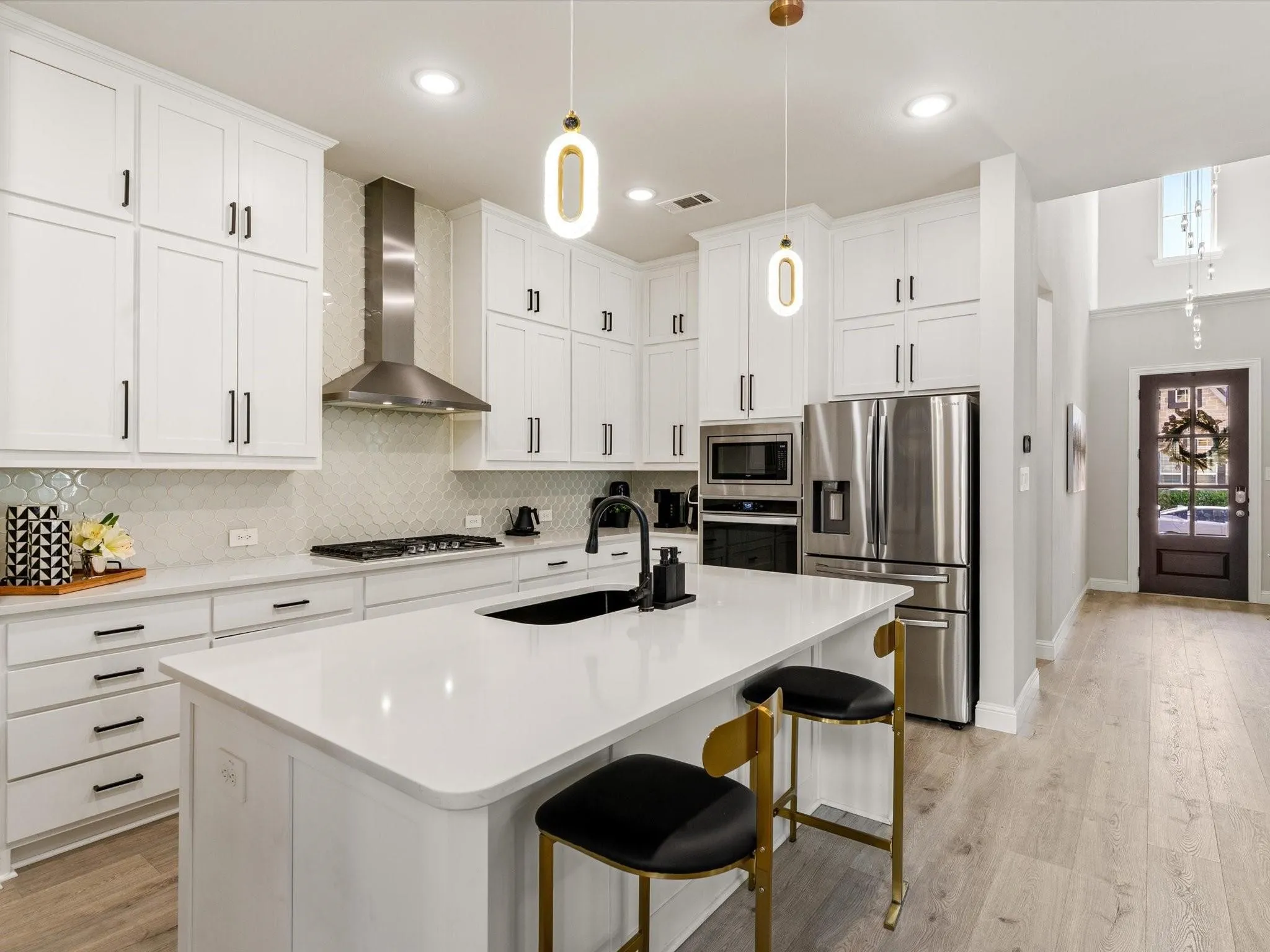 Bright kitchen featuring white shaker cabinetry, stainless steel appliances, a center island with seating, pendant lighting, and light wood-finish flooring