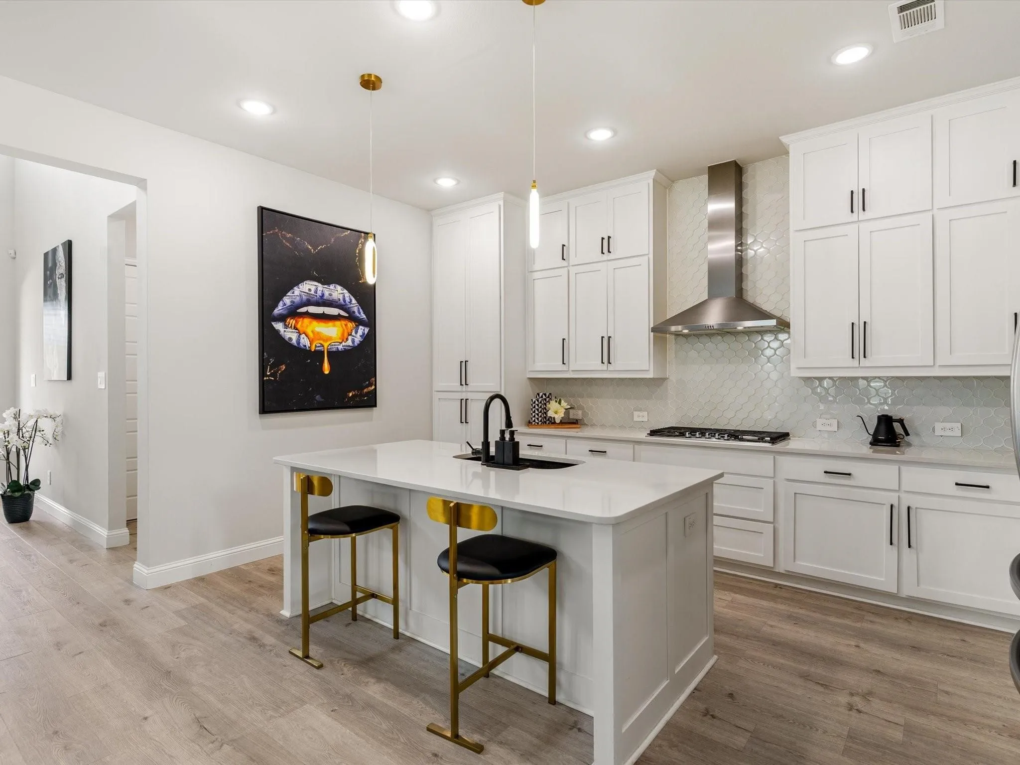 Modern kitchen featuring white shaker cabinetry, light-toned wood-finish flooring, a central island with a white countertop, and a stainless steel range hood