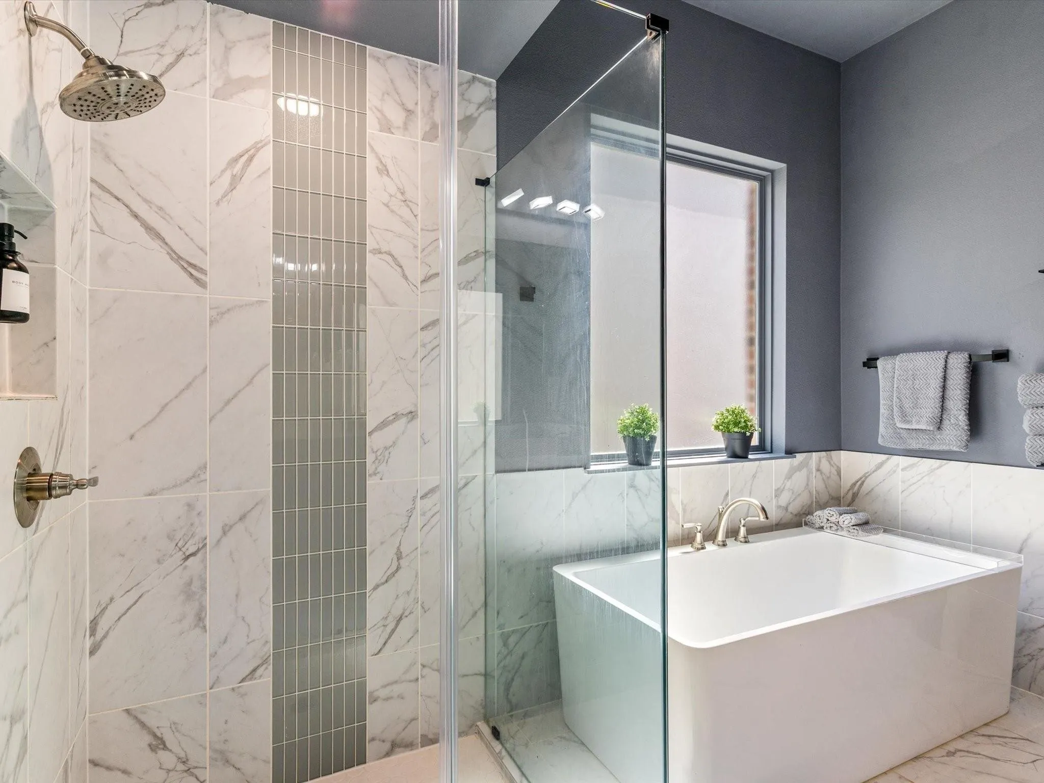 Contemporary bathroom featuring a freestanding tub with deck-mounted faucet, an enclosed shower with rain showerhead, and a window for natural light