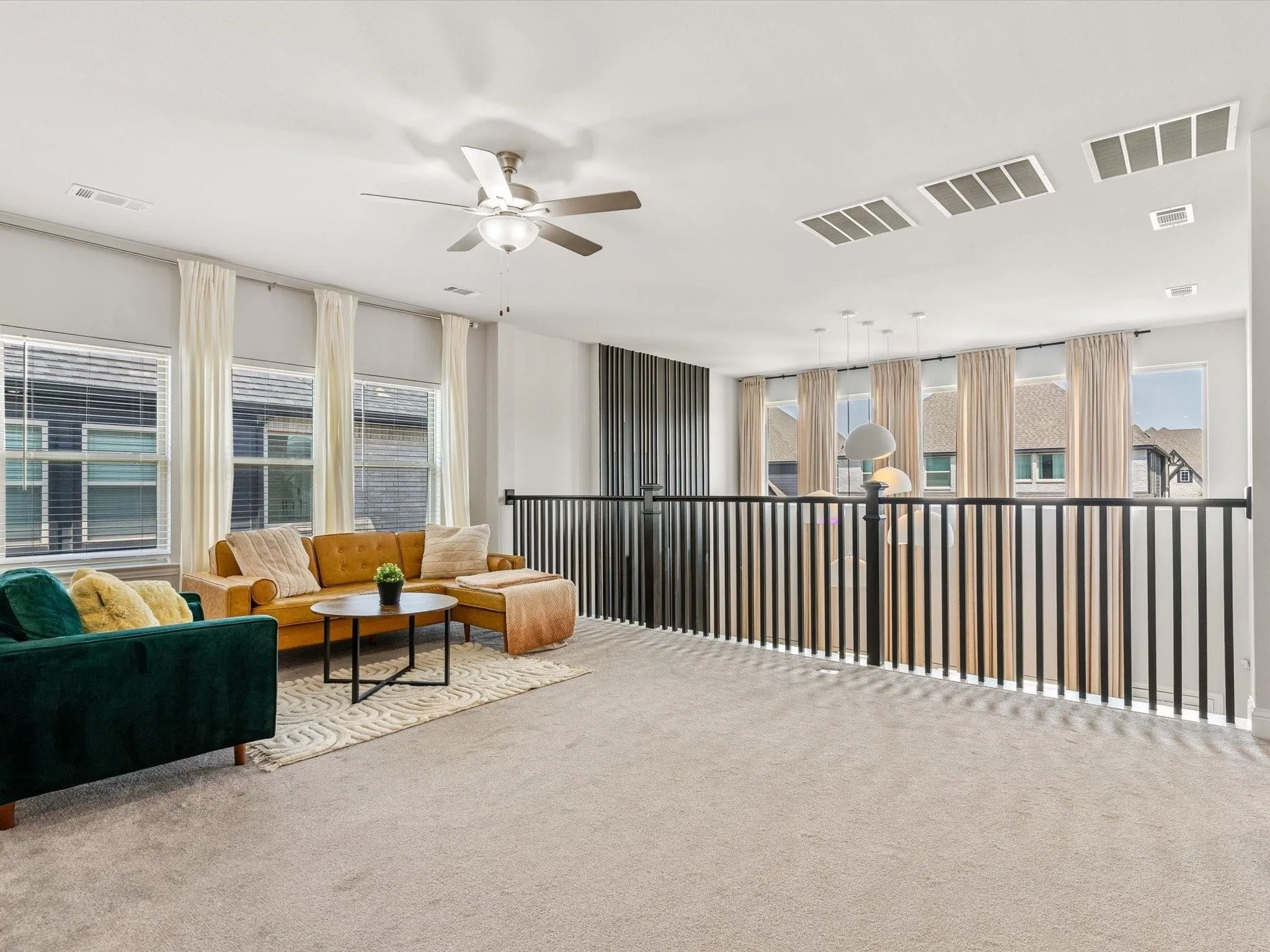 Carpeted loft area featuring a ceiling fan with integrated lighting, multiple windows with blinds, and a durable black metal railing