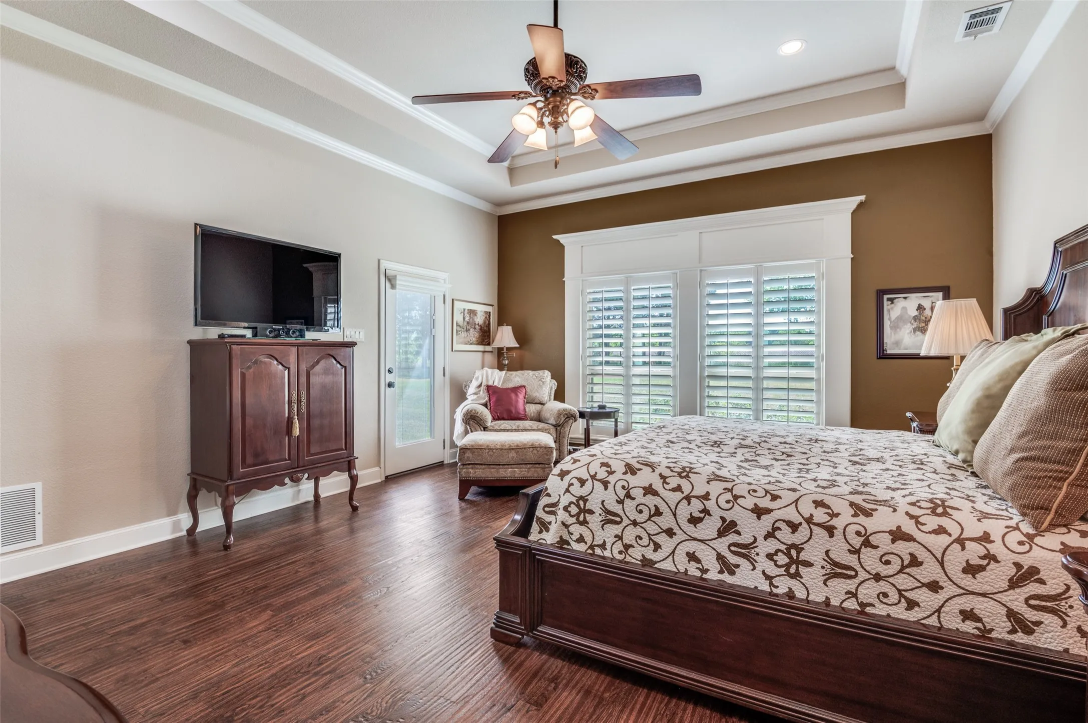 Another view of primary suite. Tray ceiling, fan, wide baseboards, views of backyard.