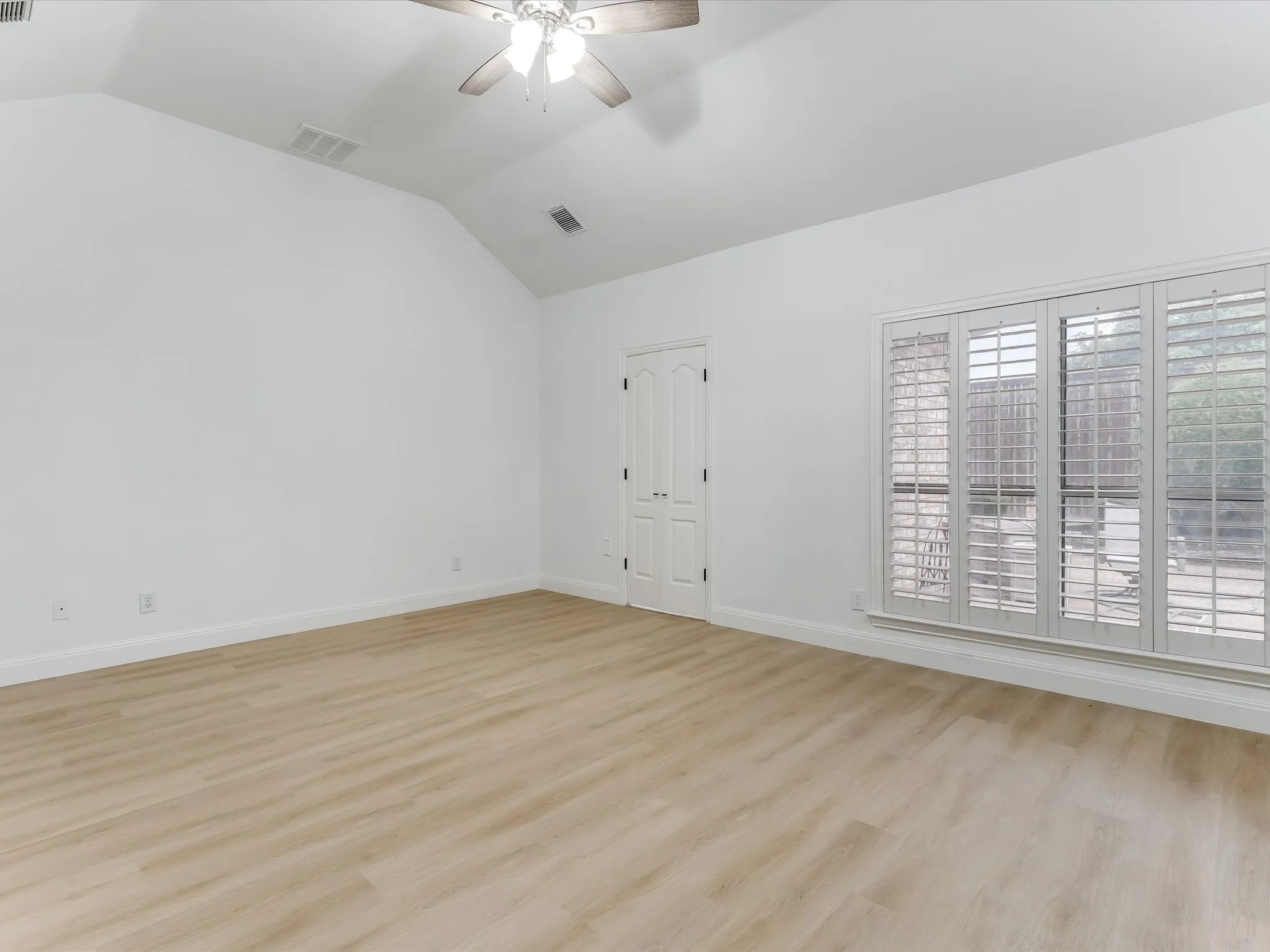 Spacious room with wood-finish flooring, vaulted ceiling, and an integrated ceiling fan