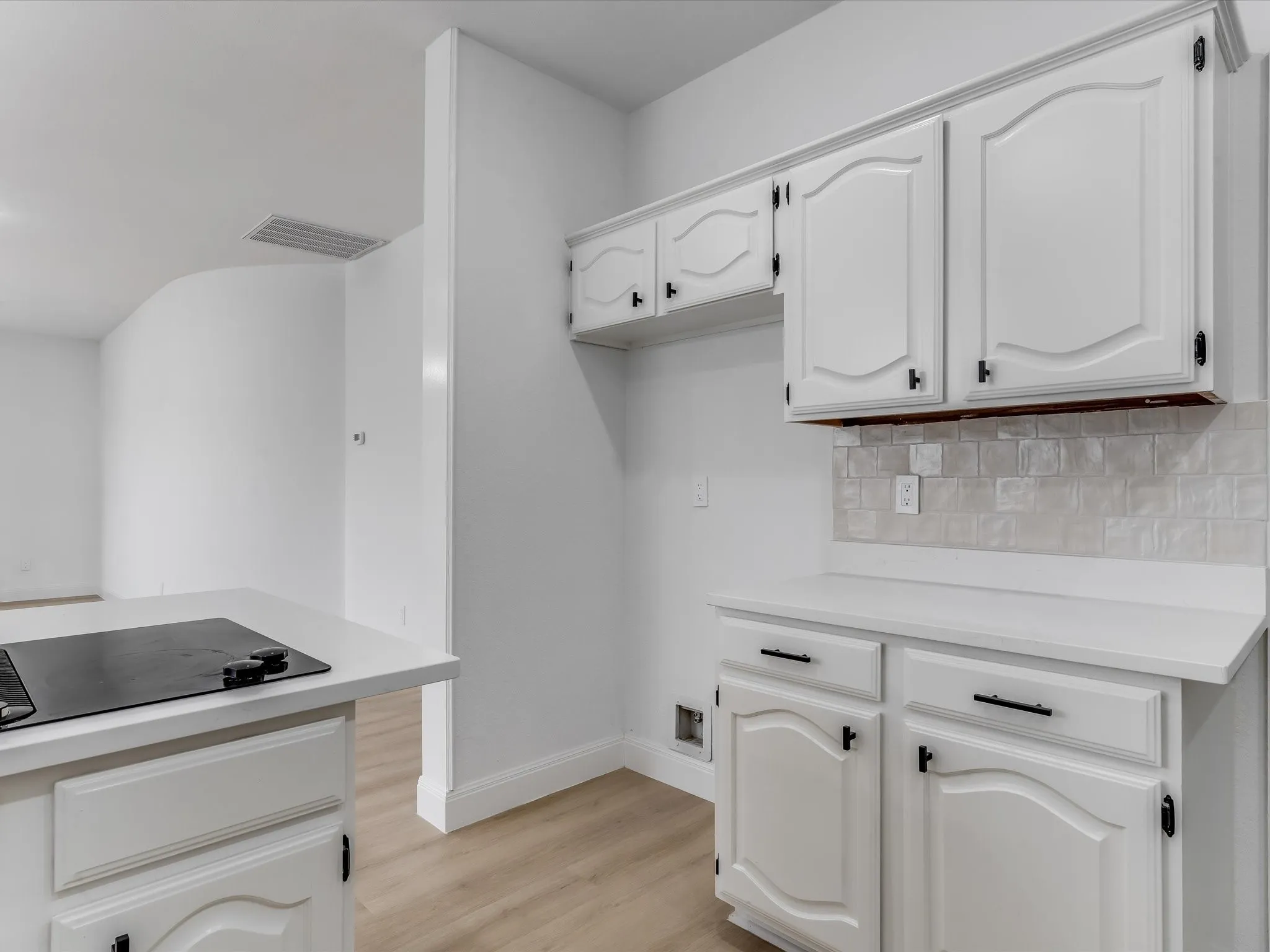 Kitchen featuring white cabinetry with black hardware, white countertops, and a light-toned tile backsplash