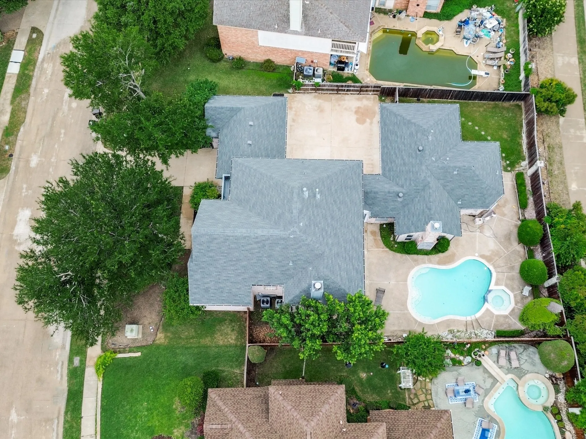 Expansive property featuring a multi-level roofline, a large backyard swimming pool with an integrated spa, concrete patio space, and mature trees providing natural landscaping