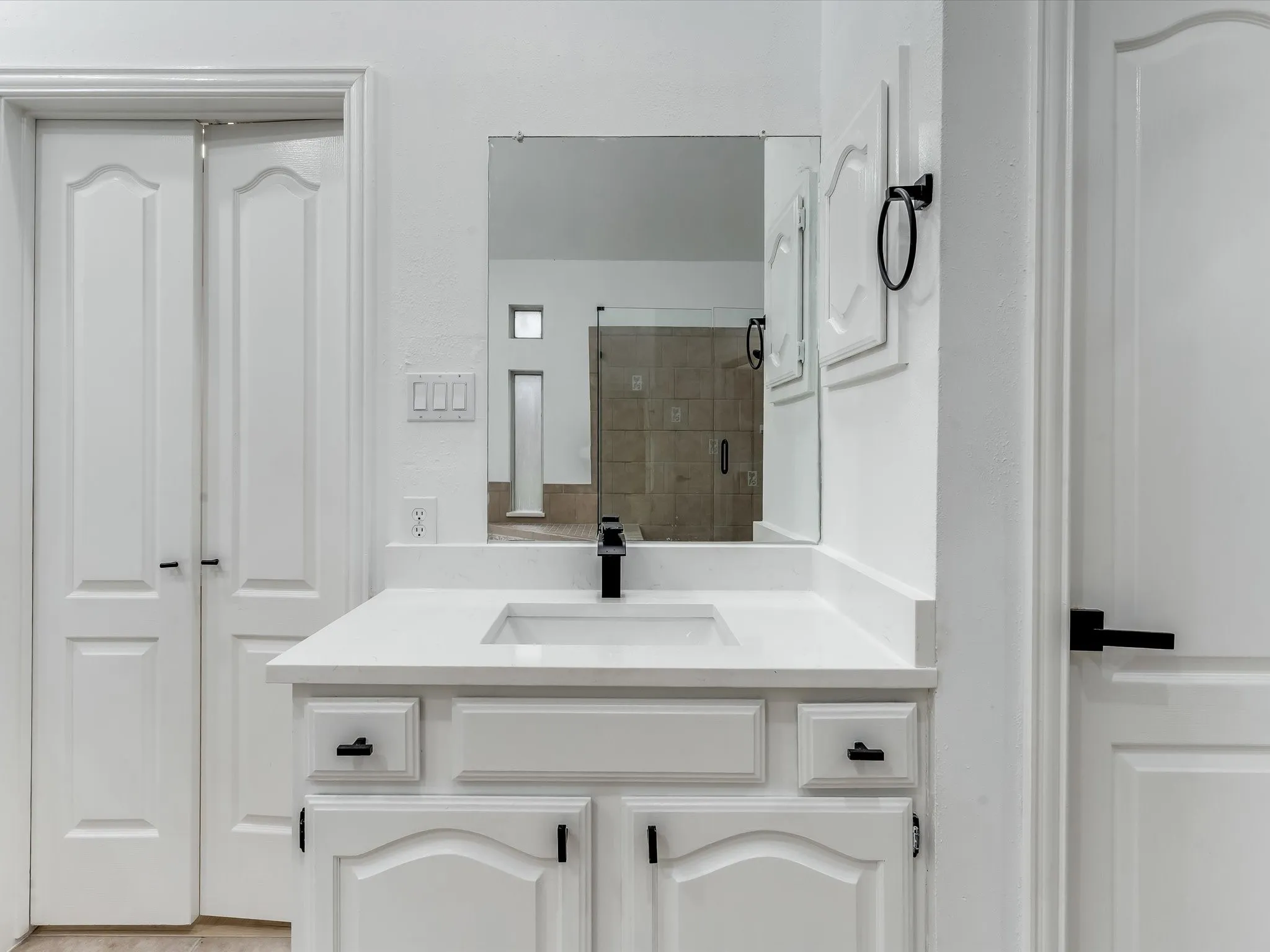 Bathroom vanity featuring a white countertop with an integrated sink, matte black faucet, and white cabinetry