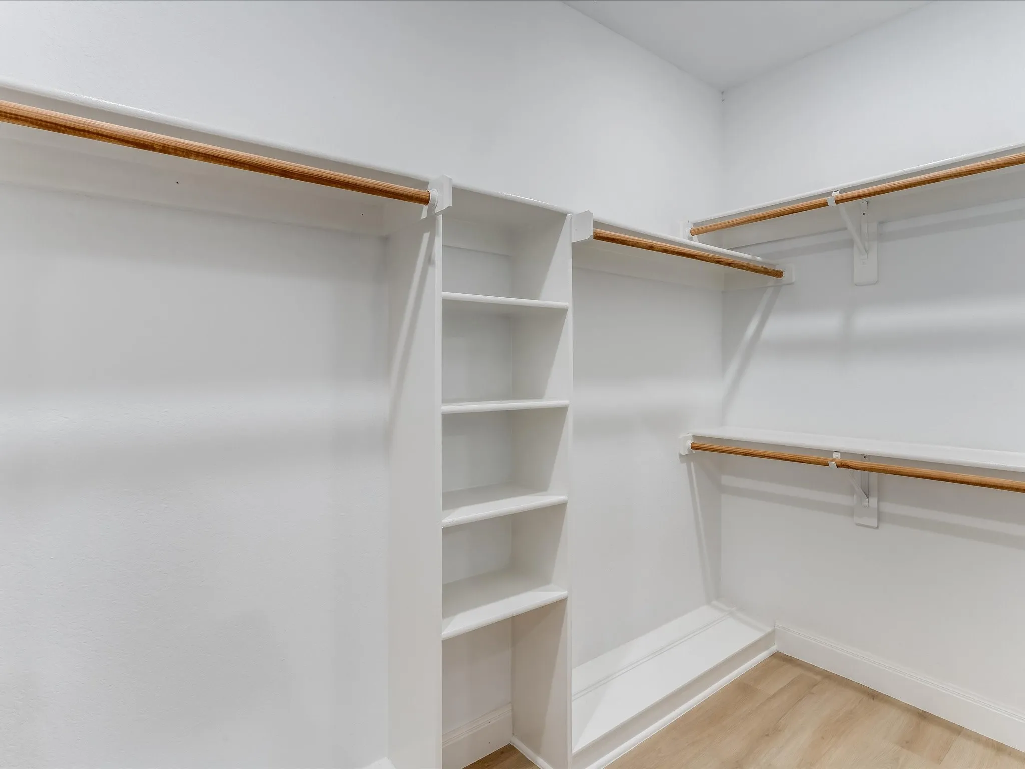 Walk-in closet featuring built-in shelving, multiple hanging rods, white trim, and wood-finish flooring