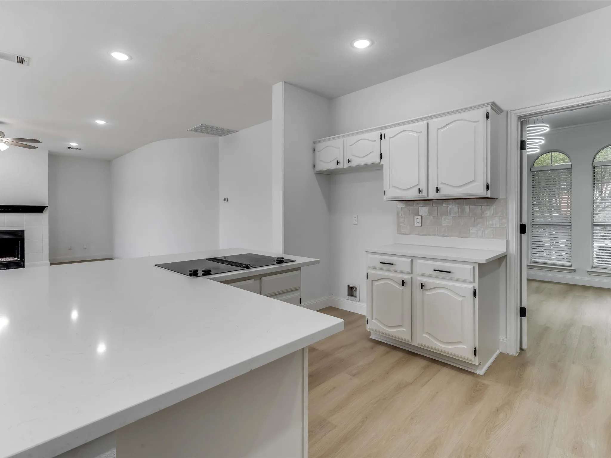 Kitchen featuring a large island with an integrated cooktop, white cabinetry, light countertops, and a tiled backsplash