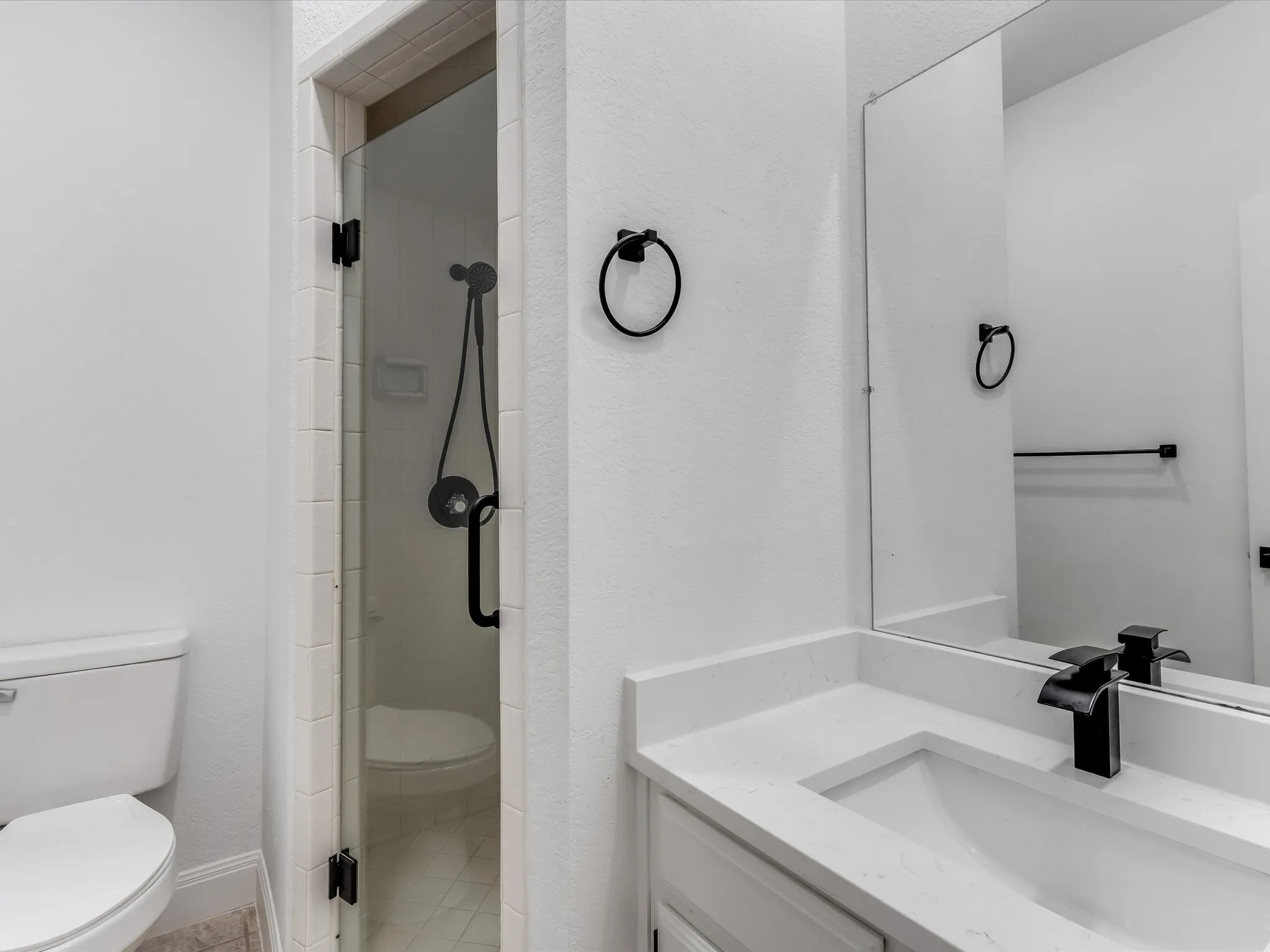 Contemporary bathroom featuring a frameless glass shower enclosure with matte black hardware, a shower head with an attached sprayer, a white vanity with an integrated sink, a quartz countertop, and a matte black faucet