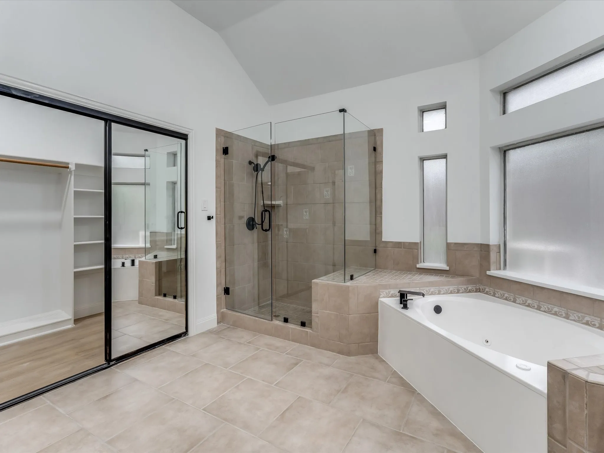 Bathroom featuring a corner soaking tub, a glass-enclosed shower with tiled walls, and light-toned tile flooring