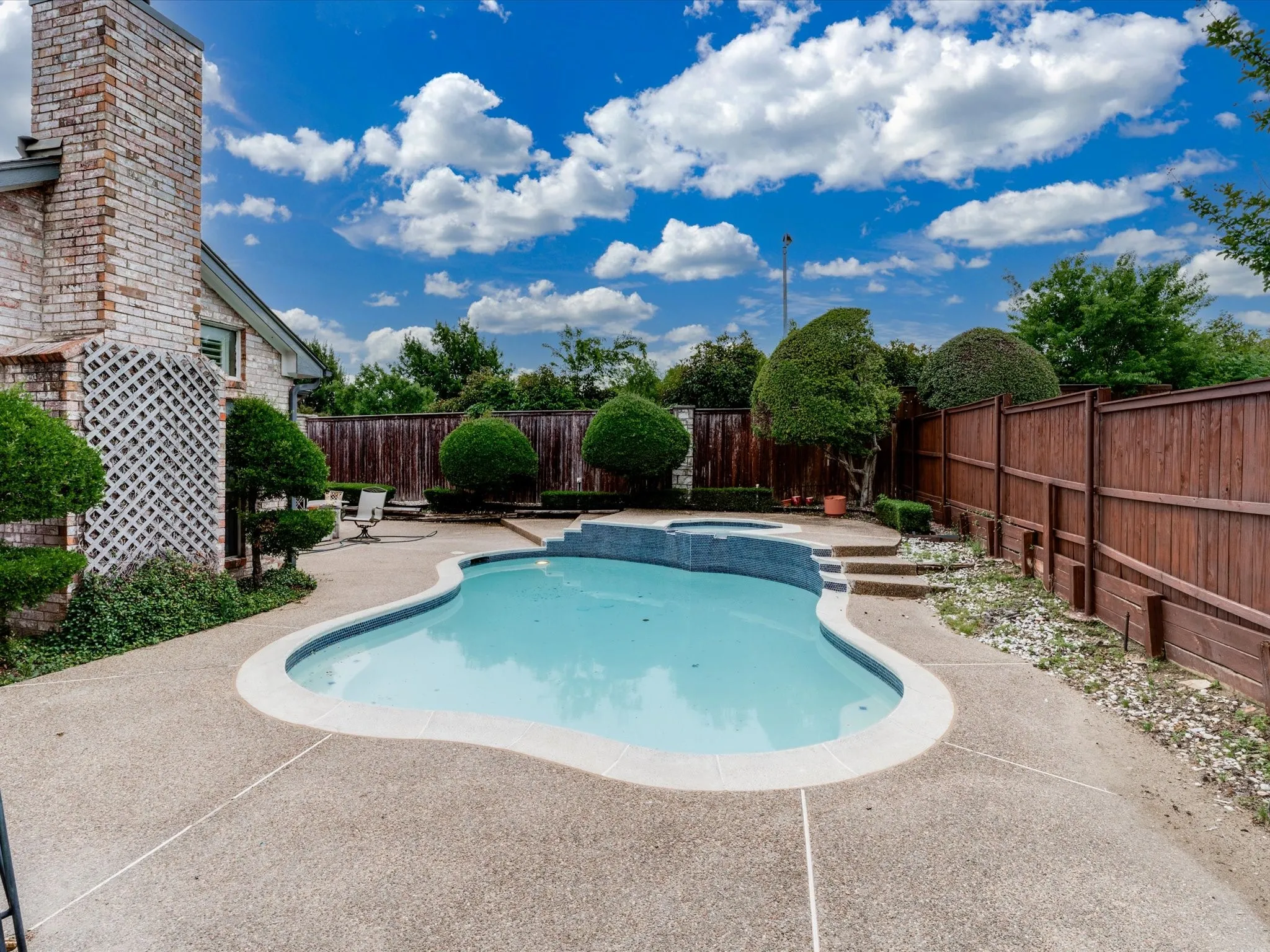 Outdoor oasis featuring a freeform swimming pool with integrated spa and aggregate concrete decking