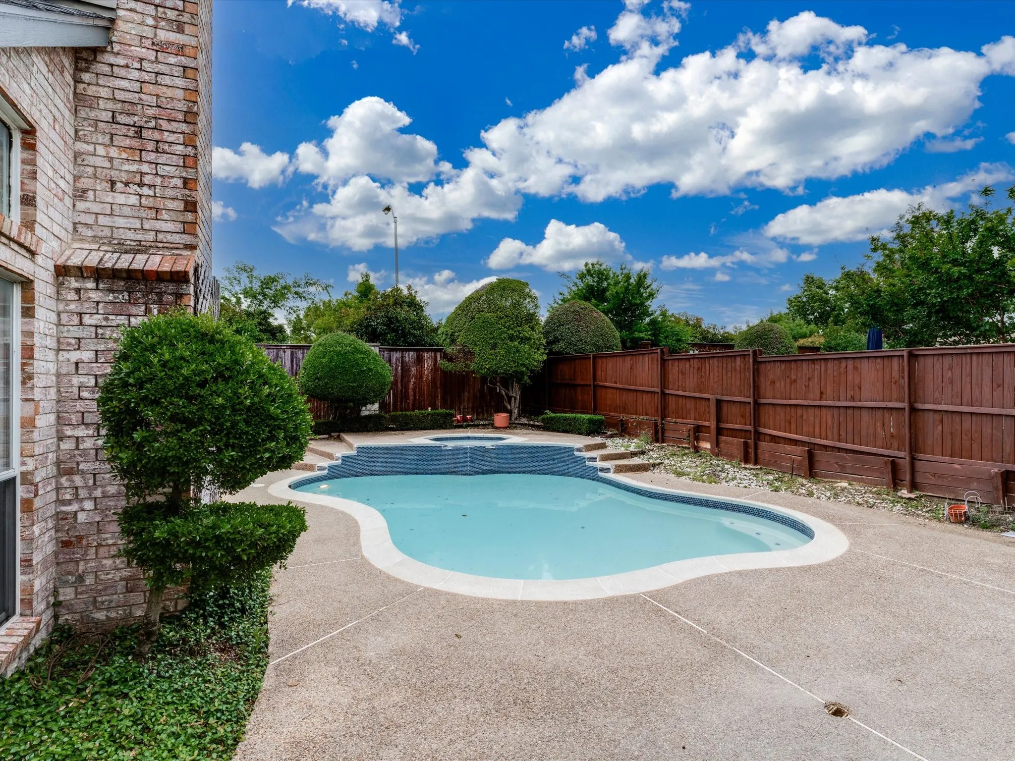 Kidney-shaped swimming pool featuring an integrated spa with tiled steps