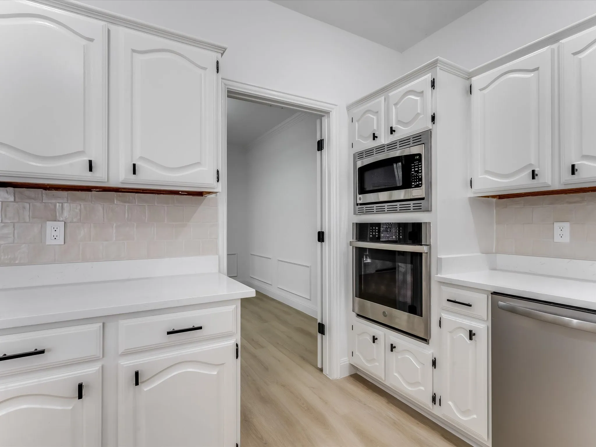 White cabinetry with black hardware, complementing white countertops, and a light-toned tile backsplash