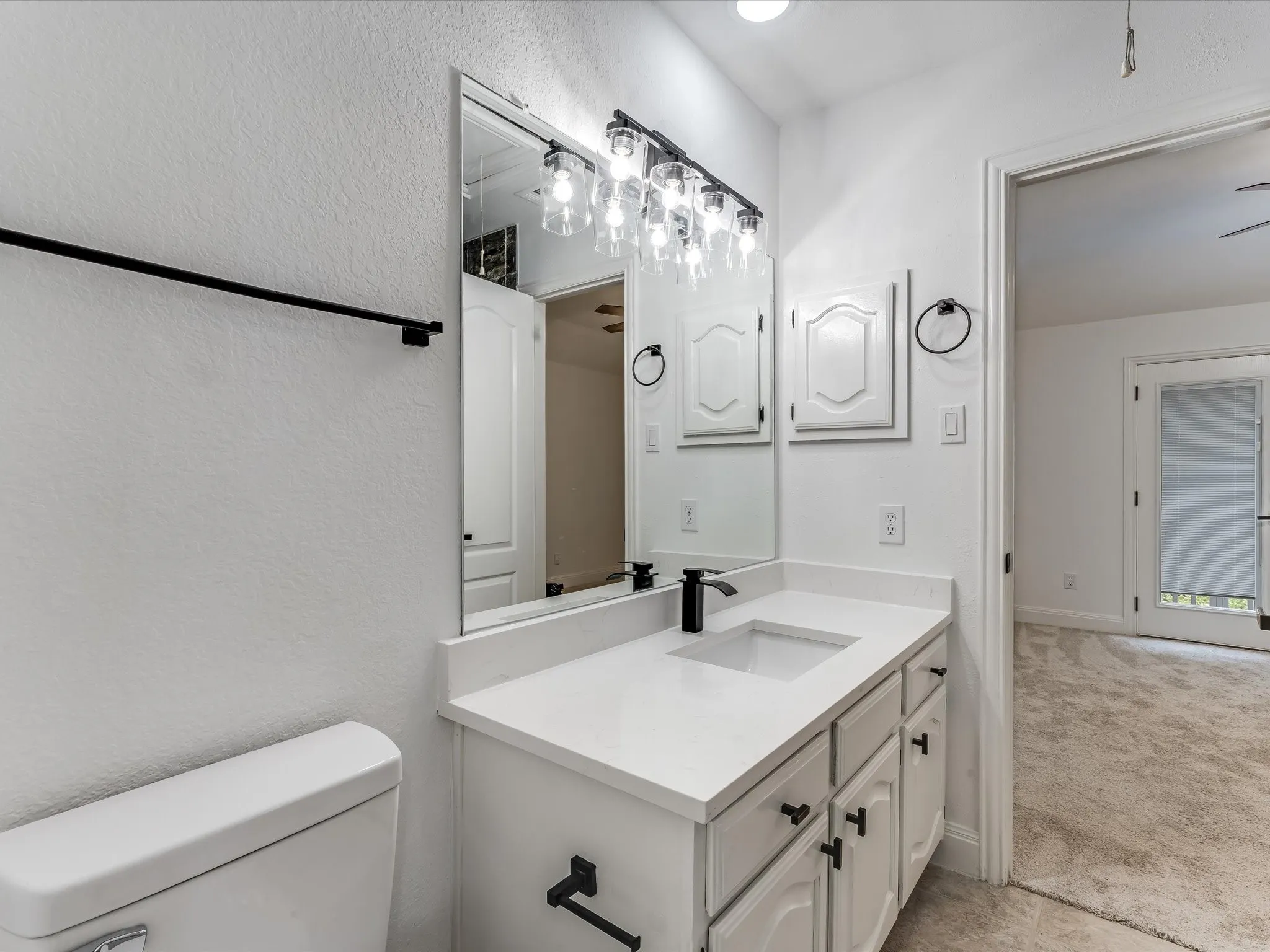 Bathroom vanity featuring a single sink, white countertop, white cabinetry with black hardware, and an overhead light fixture