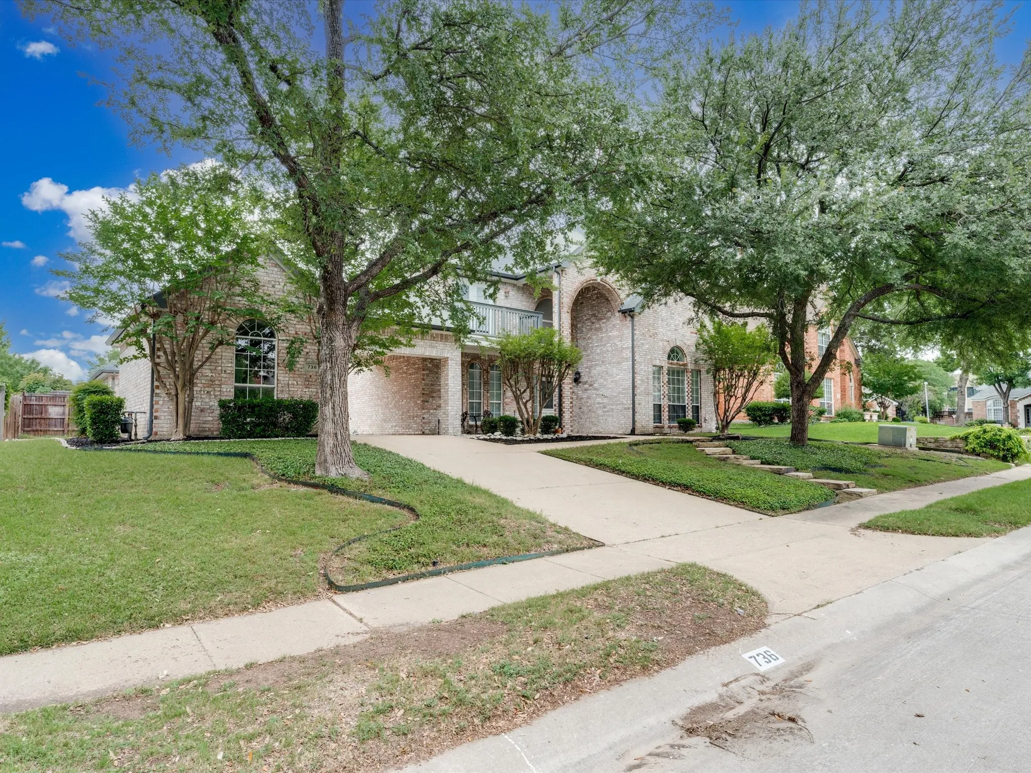 Traditional brick exterior featuring a covered entry, arched window accents, mature trees, and a concrete driveway