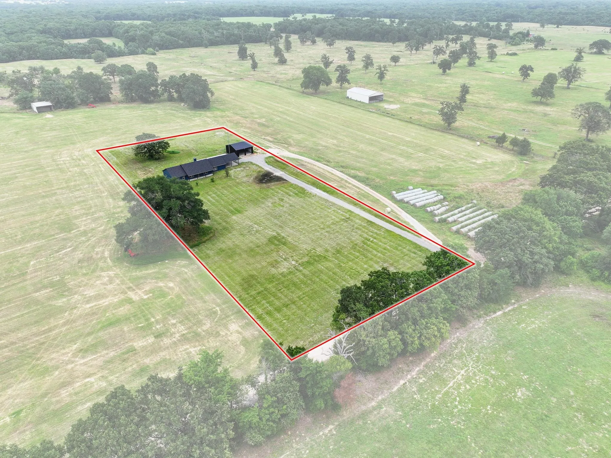 Expansive land parcel featuring a main residence with dark siding, a detached garage, and a long driveway
