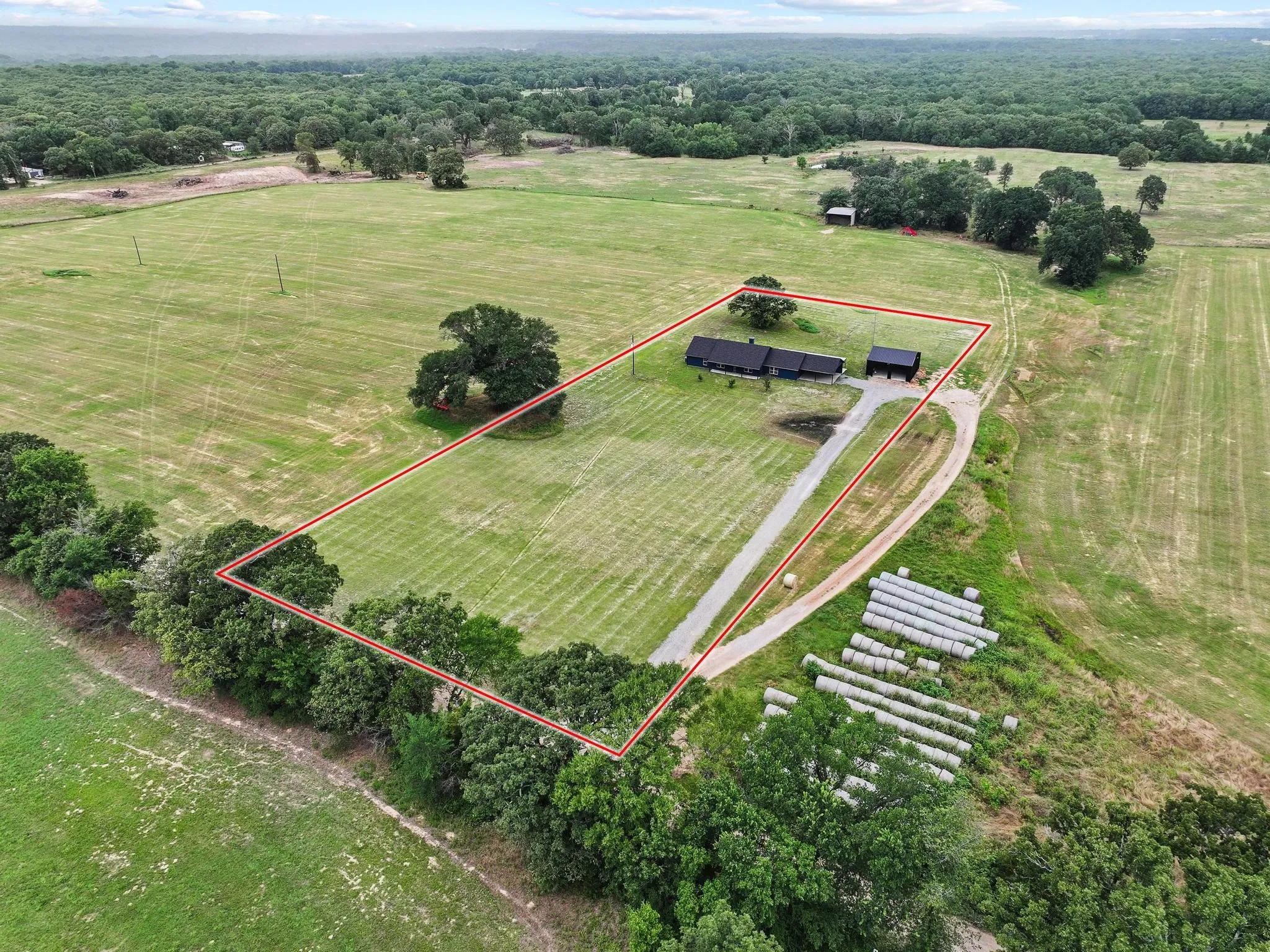 Expansive agricultural property featuring a lengthy gravel driveway, a single-story dwelling, and a separate outbuilding