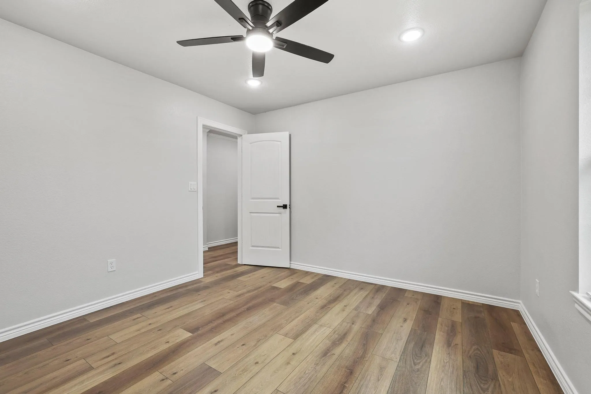 Light-filled room featuring wood-finish flooring and a contemporary ceiling fan