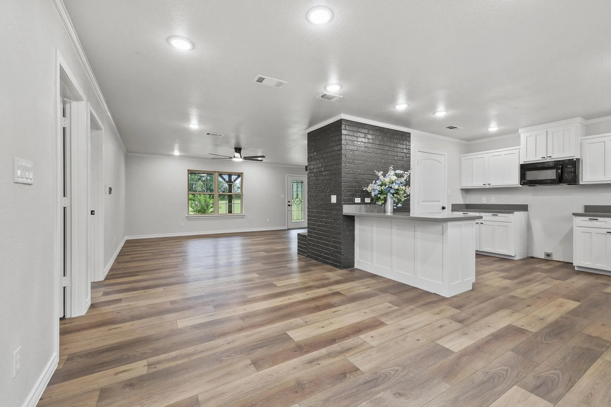 Open-concept living space featuring wood-finish flooring, recessed lighting, a modern ceiling fan, and a kitchen with white cabinetry and dark countertops