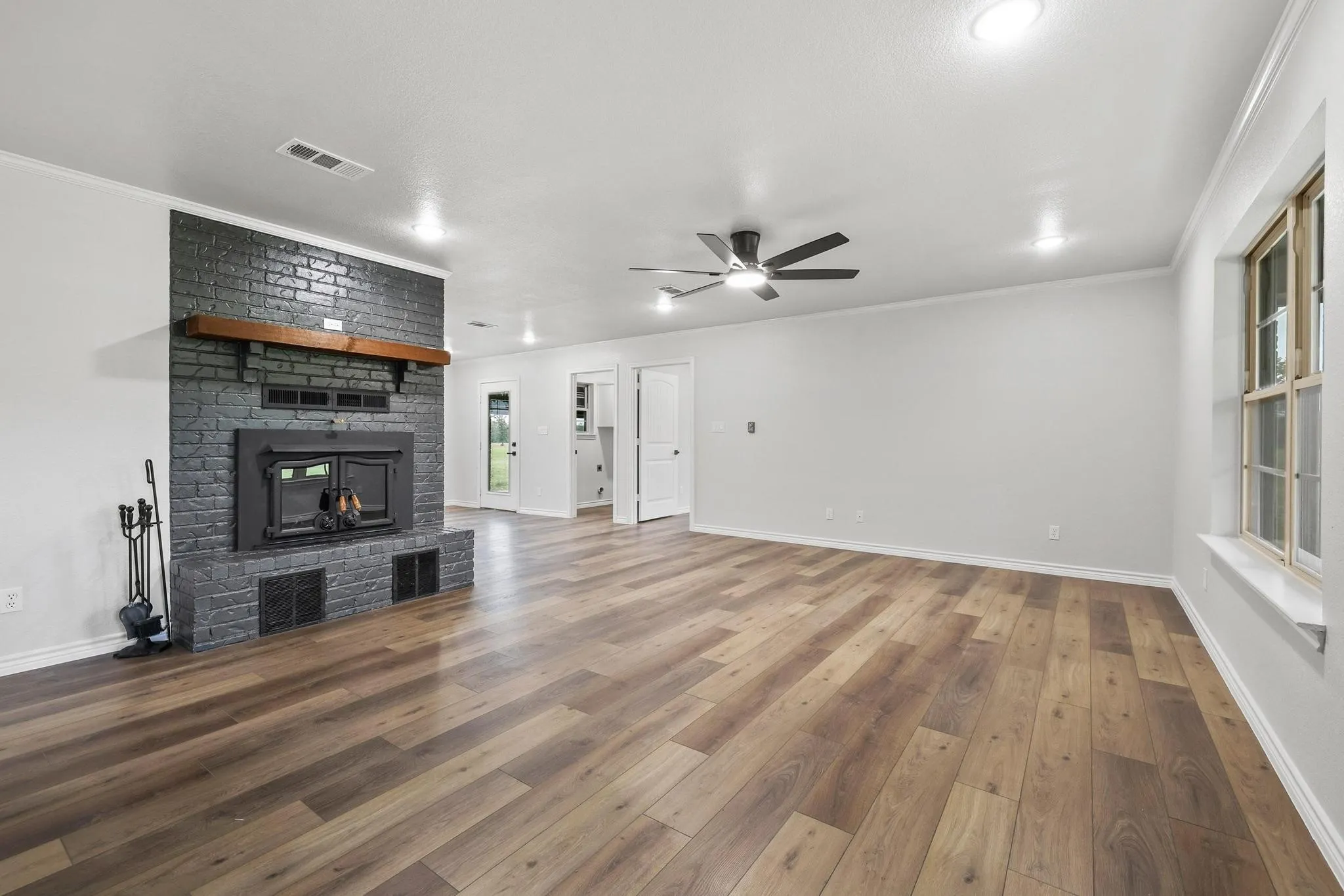 Spacious room featuring a dark brick fireplace with a wood mantle, wood-finish flooring, a ceiling fan, recessed lighting, and white trim