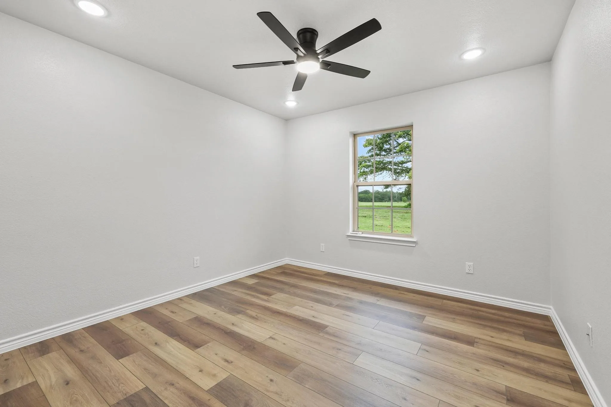 Bright room with wood-finish flooring, white baseboards, and a single window