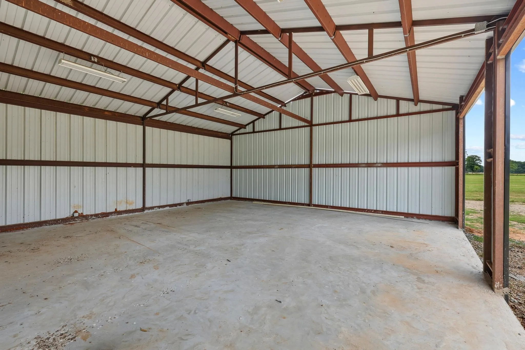 Spacious metal outbuilding with a concrete floor, exposed structural beams, corrugated metal walls, and overhead fluorescent lighting