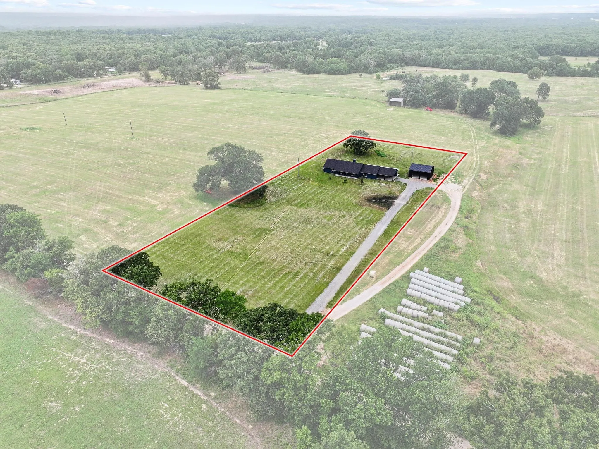 Expansive rural property featuring a main residence, detached outbuilding, a long driveway, mature trees, and a tree line border