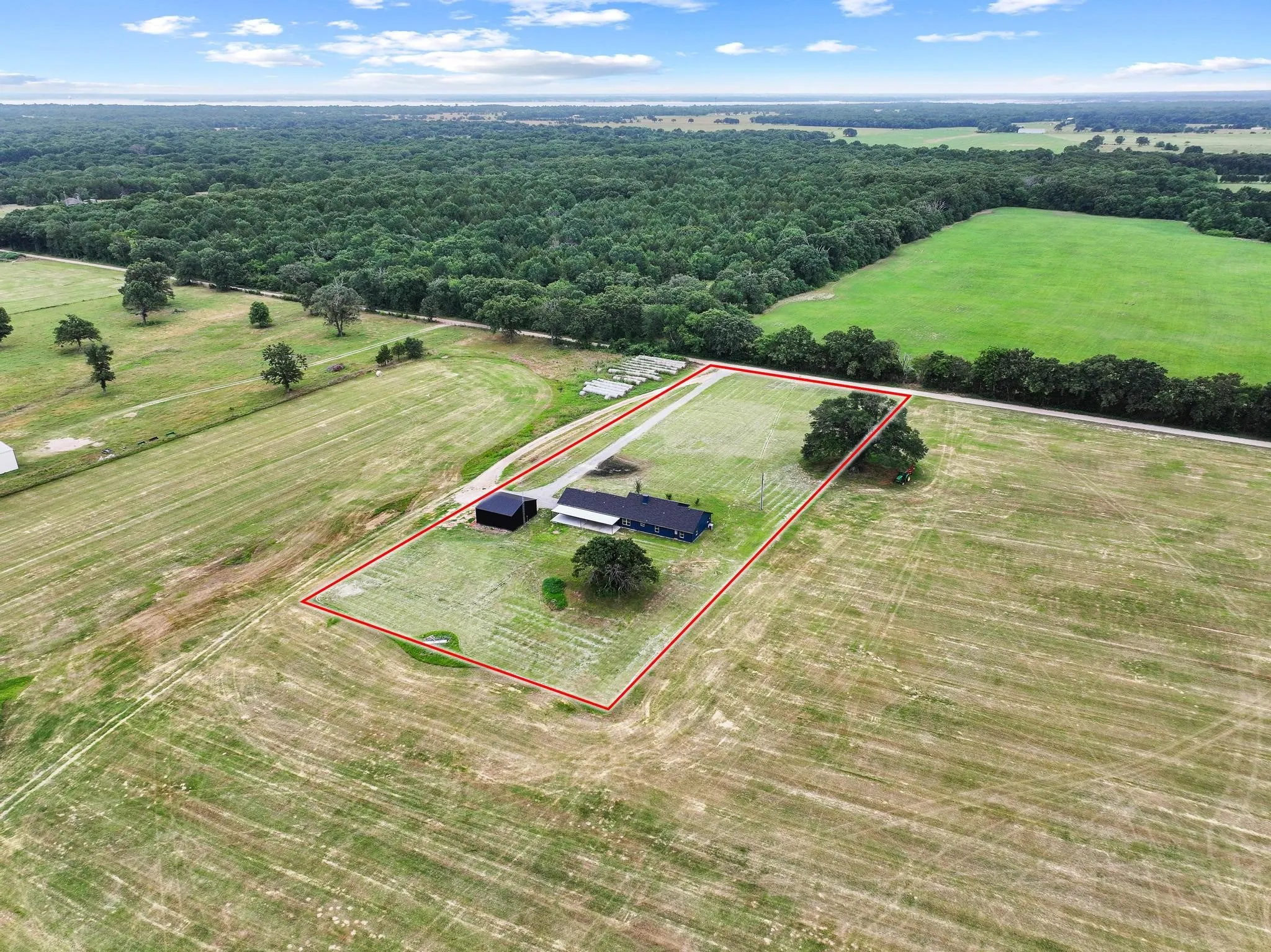 Expansive rural property featuring a primary residence, detached outbuilding, and mature trees