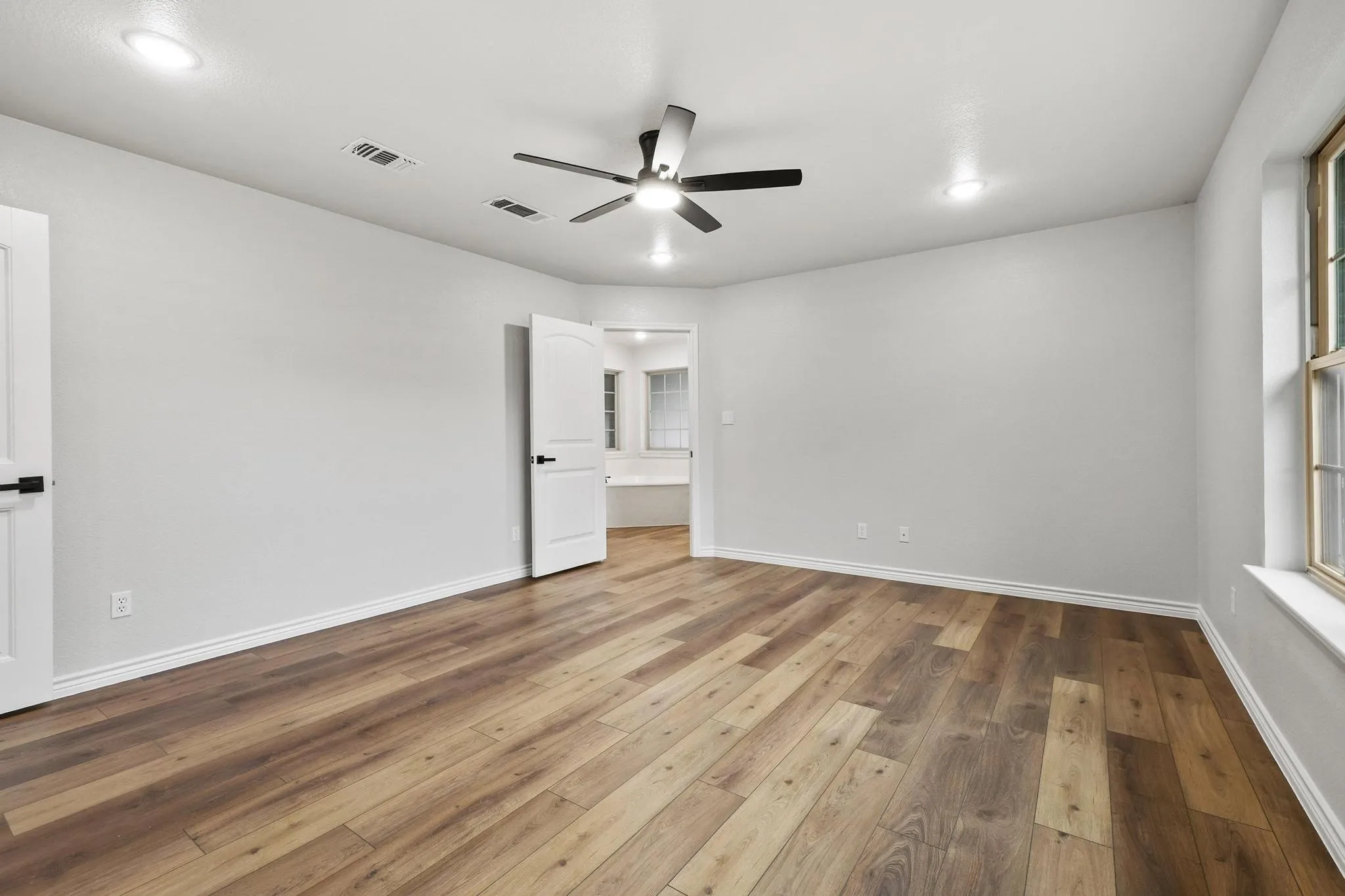 Spacious room featuring wood-finish flooring, light gray walls, a ceiling fan with integrated lighting, and recessed ceiling lights