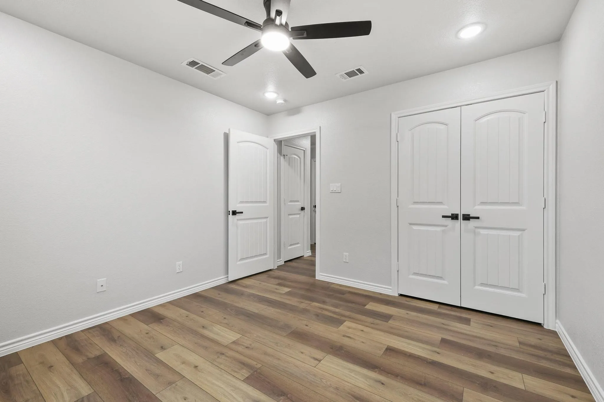 Interior room featuring wood-finish flooring, white walls, and a ceiling fan with integrated lighting