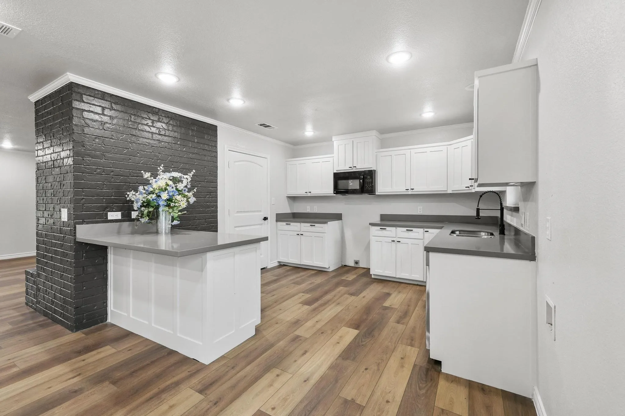 Open kitchen featuring wood-finish flooring, white cabinetry, dark countertops, a built-in microwave, and a black brick accent wall with an integrated breakfast bar