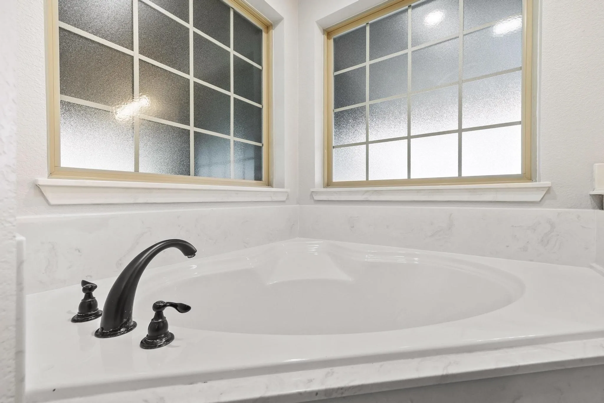 Corner soaking tub with a dark bronze faucet, surrounded by a white stone-finish deck