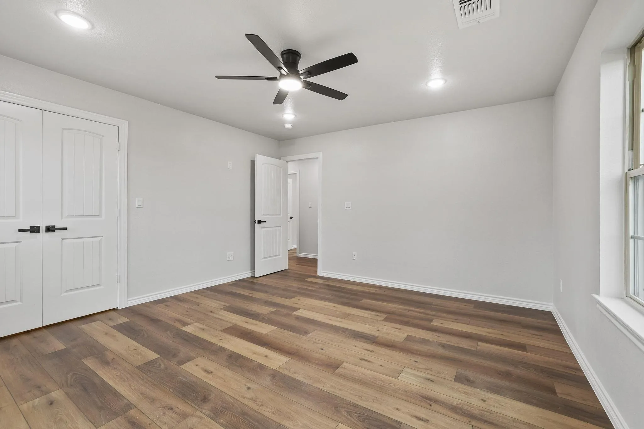 Spacious interior room featuring wood-finish flooring, white walls, and recessed lighting