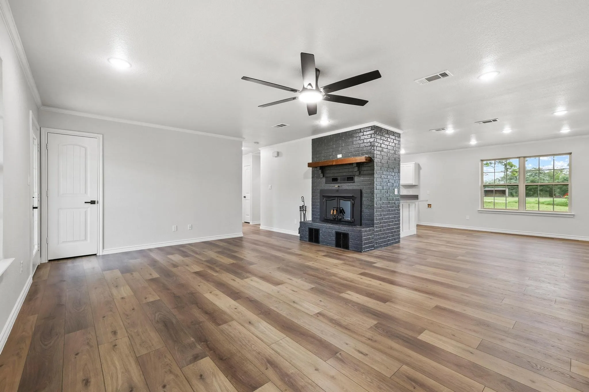 Spacious interior featuring wood-finish flooring, a painted brick fireplace with a wood mantel, a ceiling fan, and recessed lighting