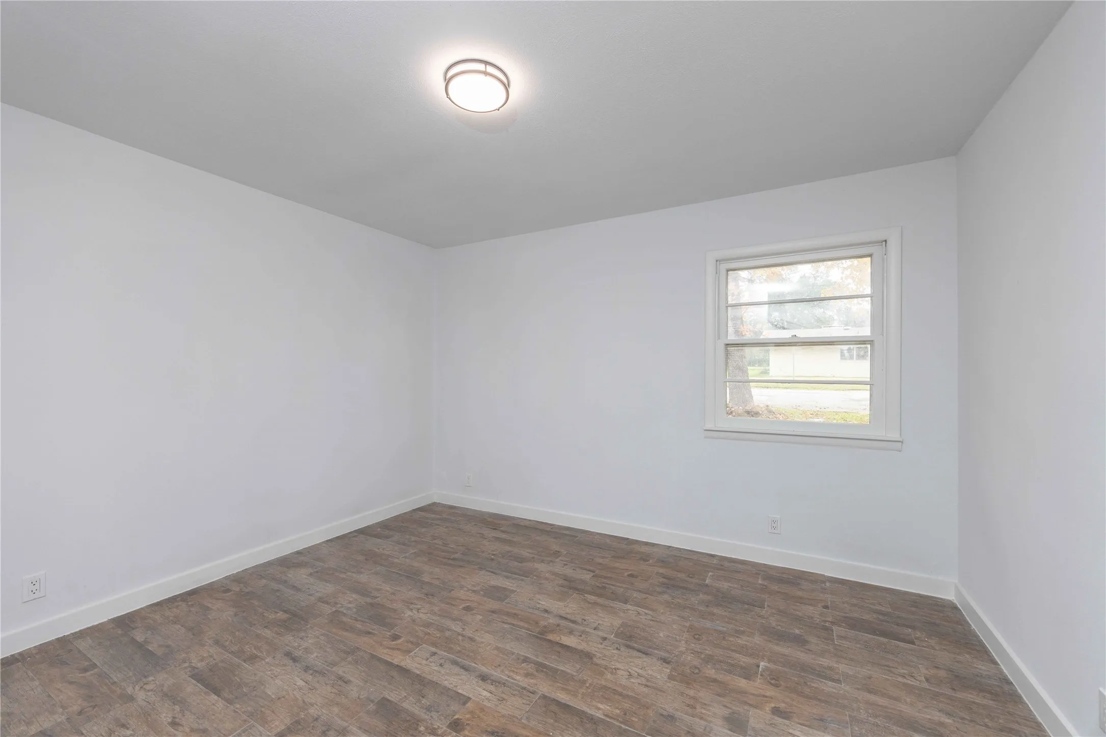 Interior room featuring wood-finish flooring, white walls, white baseboards, and a single window with white trim