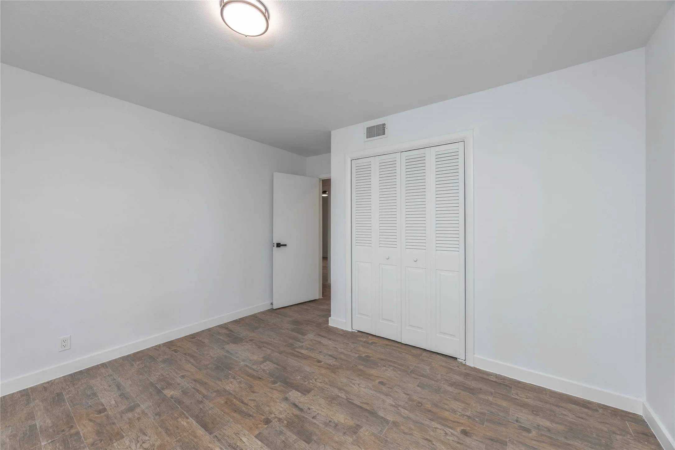 Room featuring wood-finish flooring, white walls, and a contemporary flush-mount ceiling light