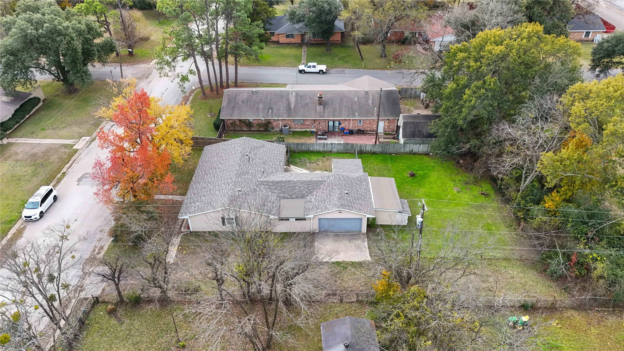 Aerial property view featuring a light-colored shingle roof, attached garage with concrete driveway, and expansive rear lawn