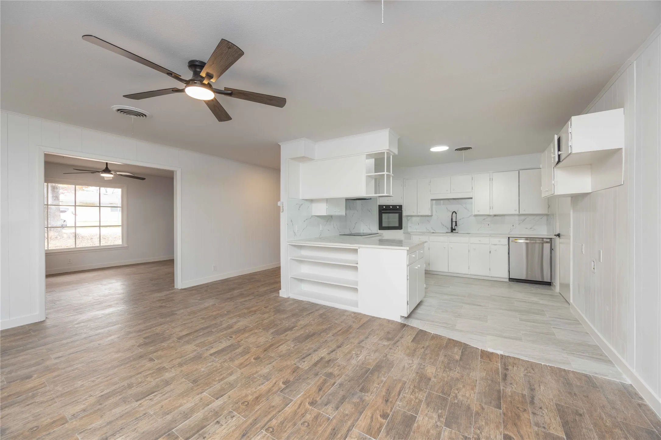 Open concept kitchen featuring an island with built-in shelving, white cabinetry, integrated oven, and stainless steel dishwasher