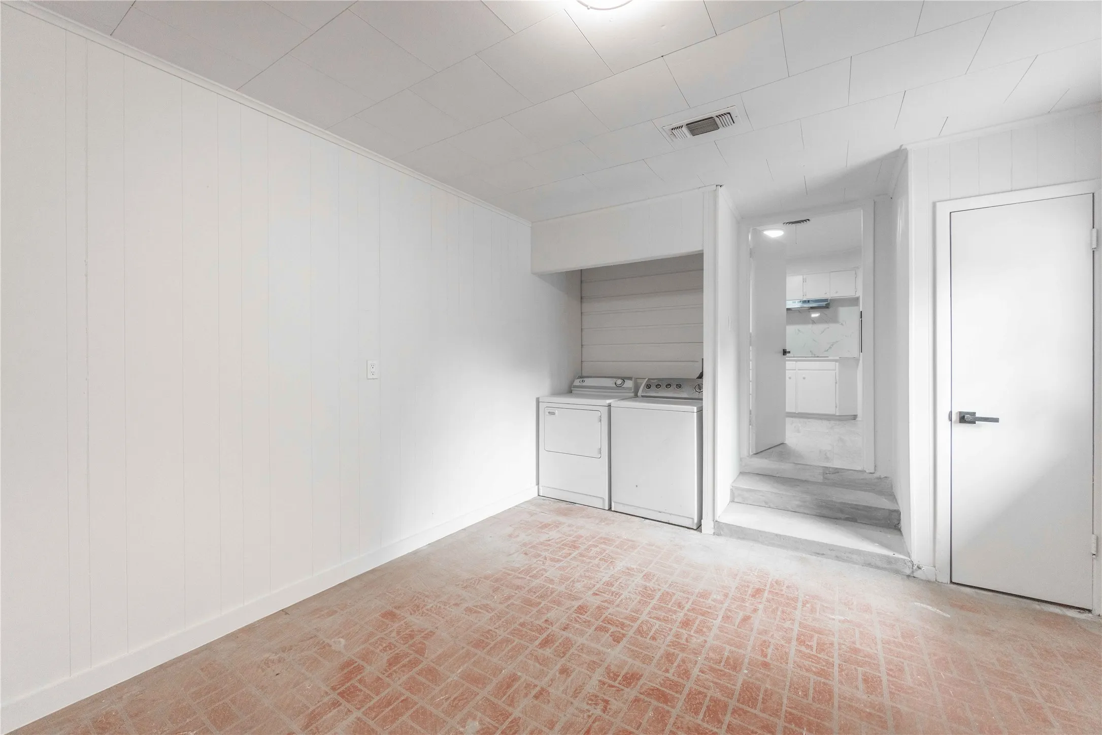 Laundry area featuring white paneling, textured ceiling, a built-in appliance alcove, and a red brick-patterned floor