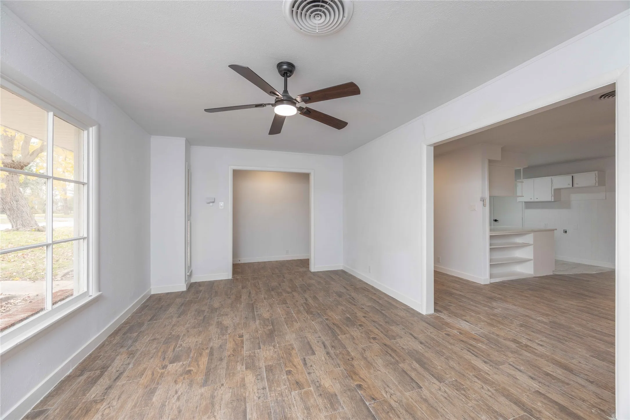 Spacious Living room featuring wood-look tile flooring, a contemporary ceiling fan with integrated lighting, and white baseboards