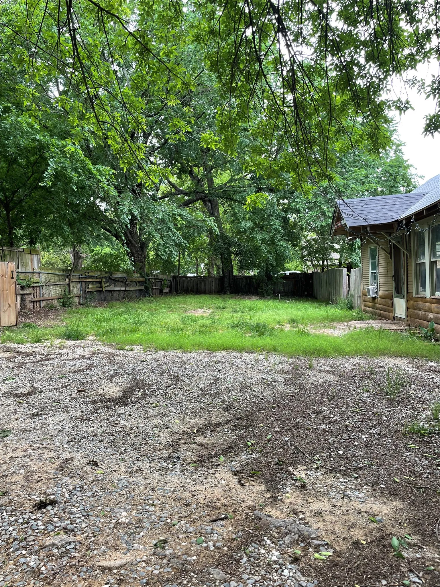 Expansive gravel area with an adjacent grassy patch, bordered by a wood fence