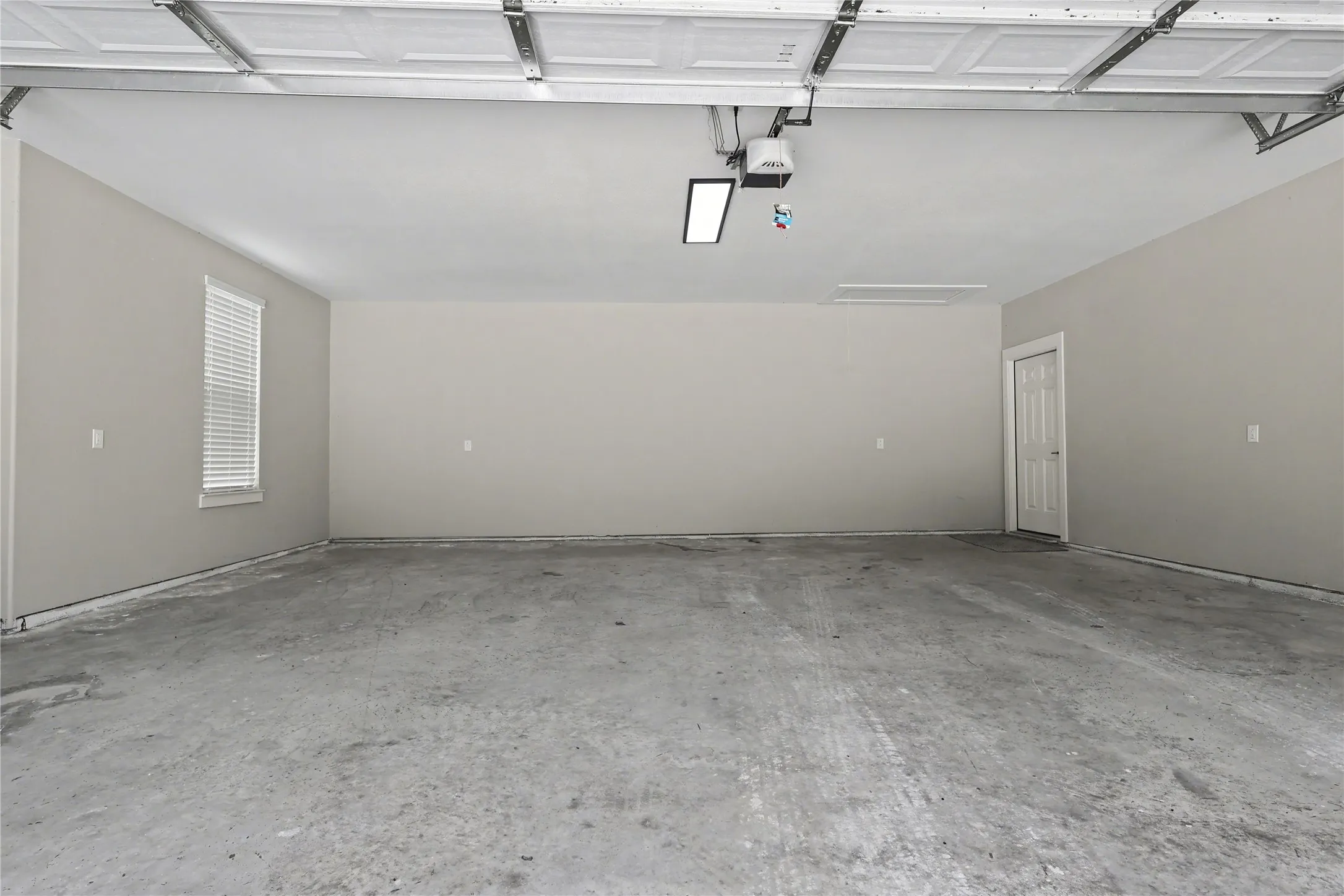Spacious garage featuring a concrete floor, light gray walls, a window with blinds, and a white interior door