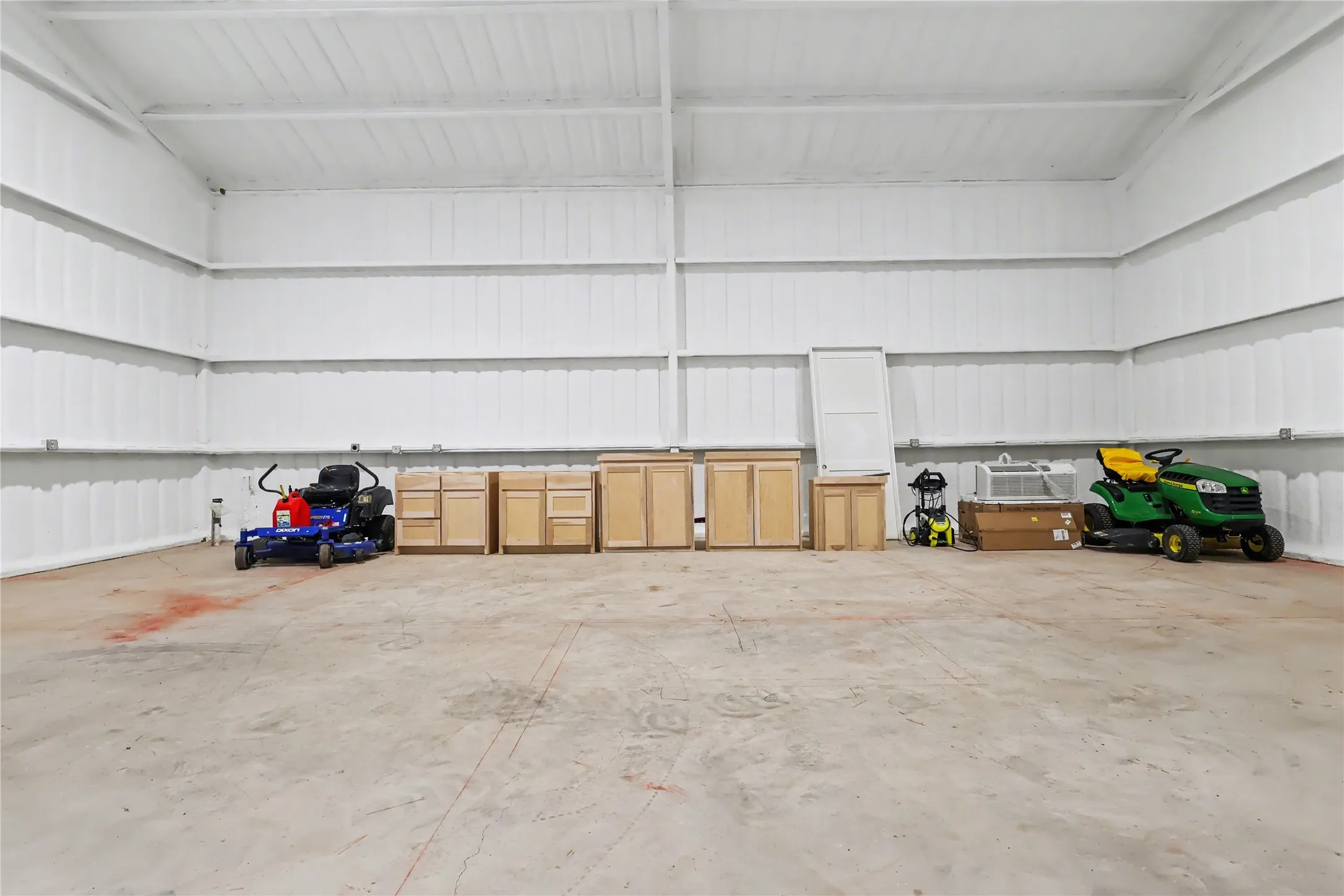 Large open shop space featuring a concrete floor, white corrugated metal walls, and a high ceiling with exposed metal beams