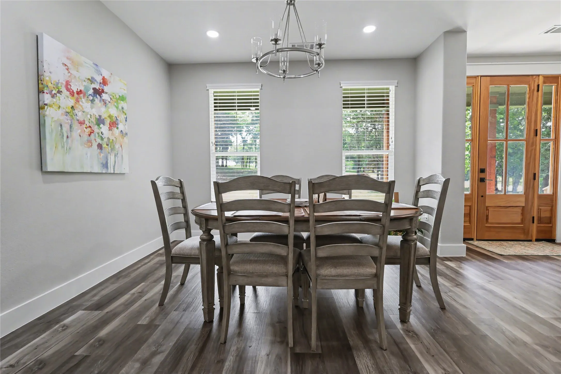 Dining area featuring wood-finish flooring, two large windows with blinds, recessed lighting, and a chandelier